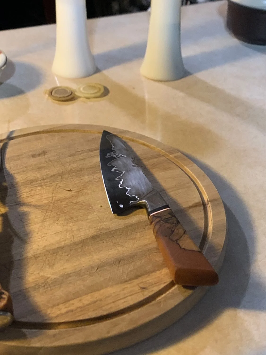 A kitchen knife with a wavy blade and wooden handle resting on a round wooden cutting board.