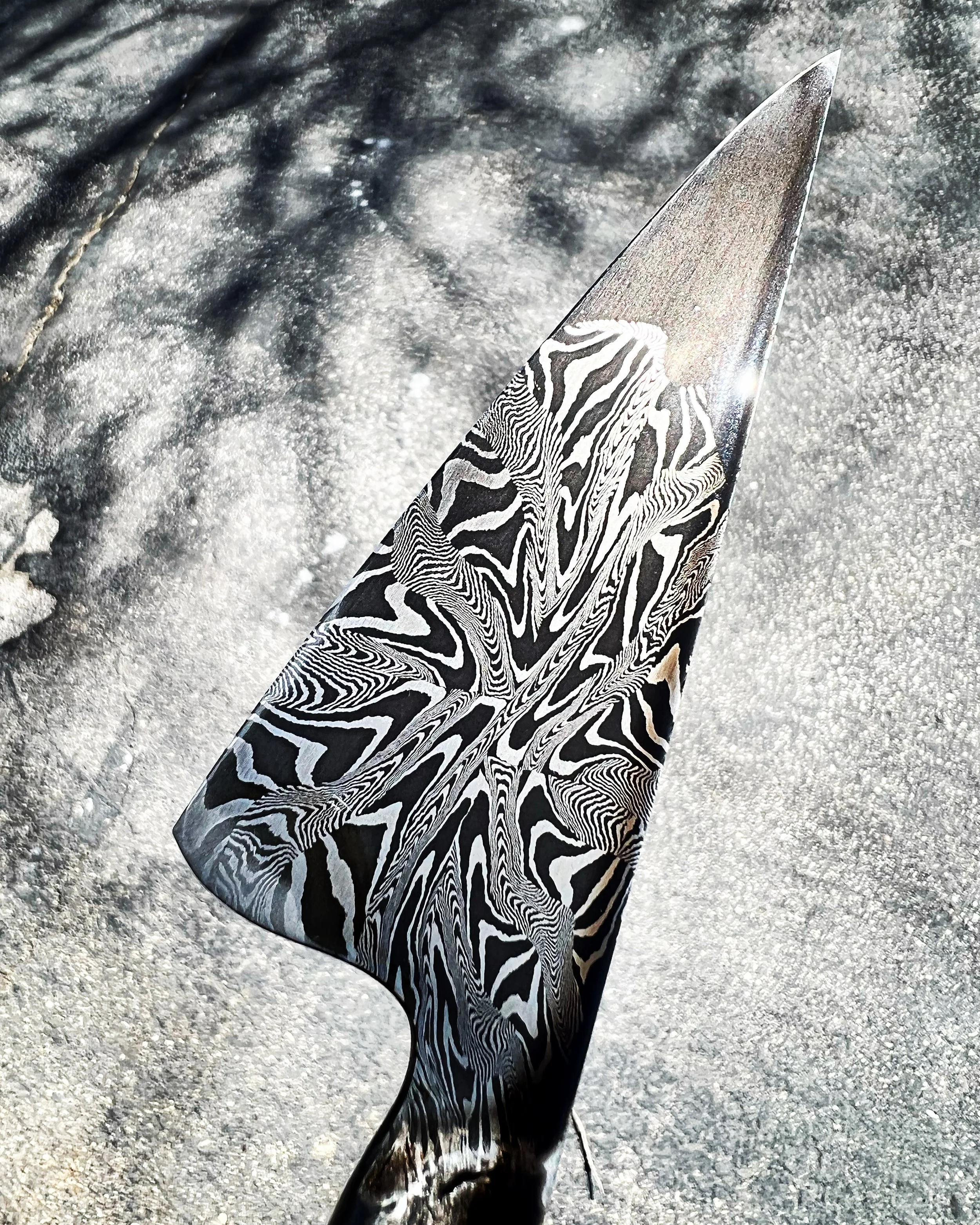 Close-up of a decorative knife with a black and white zebra stripe pattern on the blade, resting on a textured surface.