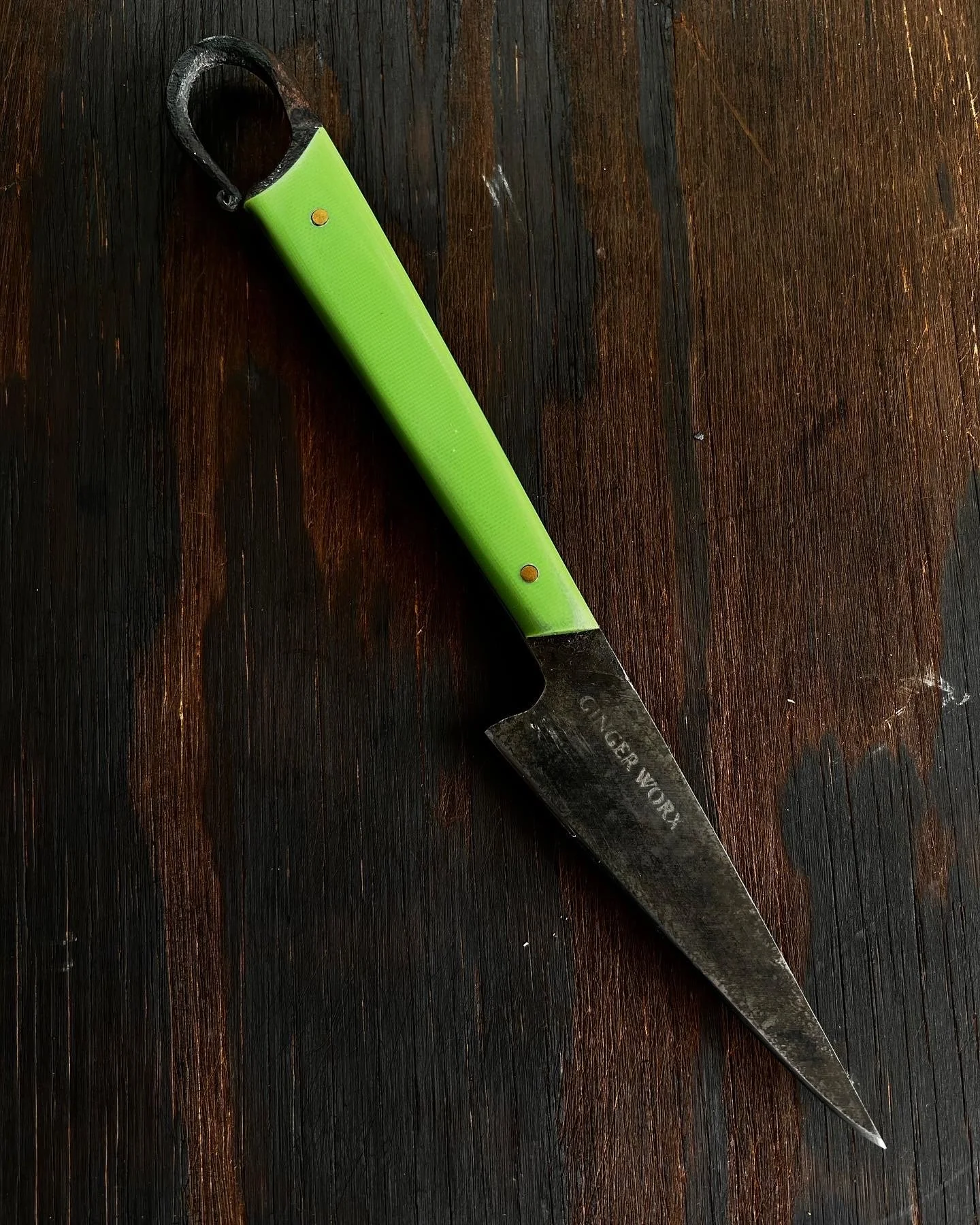 A small kitchen knife with a black blade and a bright green handle resting on a dark wooden surface.