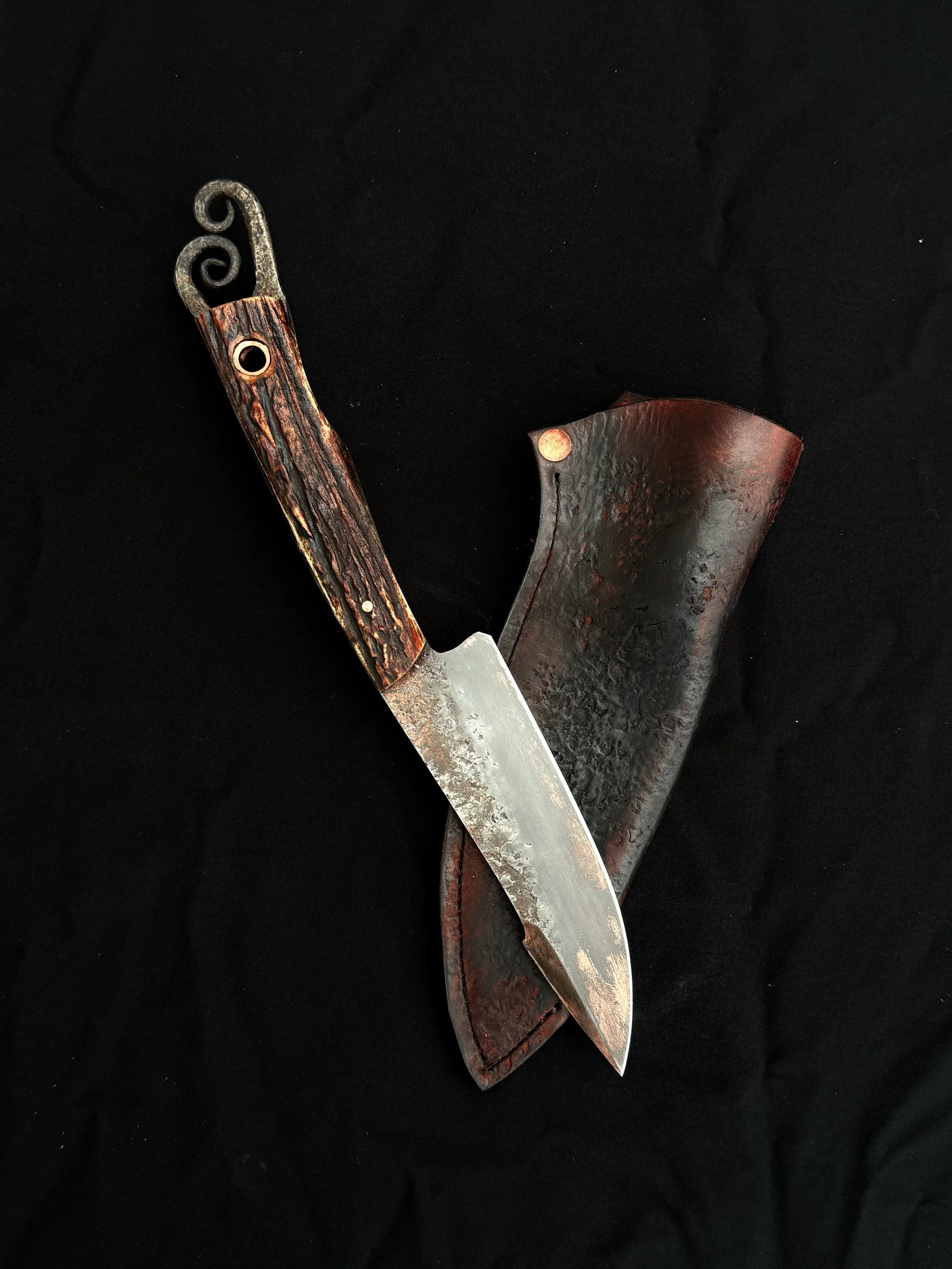 A vintage hunting knife with a textured wooden handle, a sharp blade, and a leather sheath on a black background.