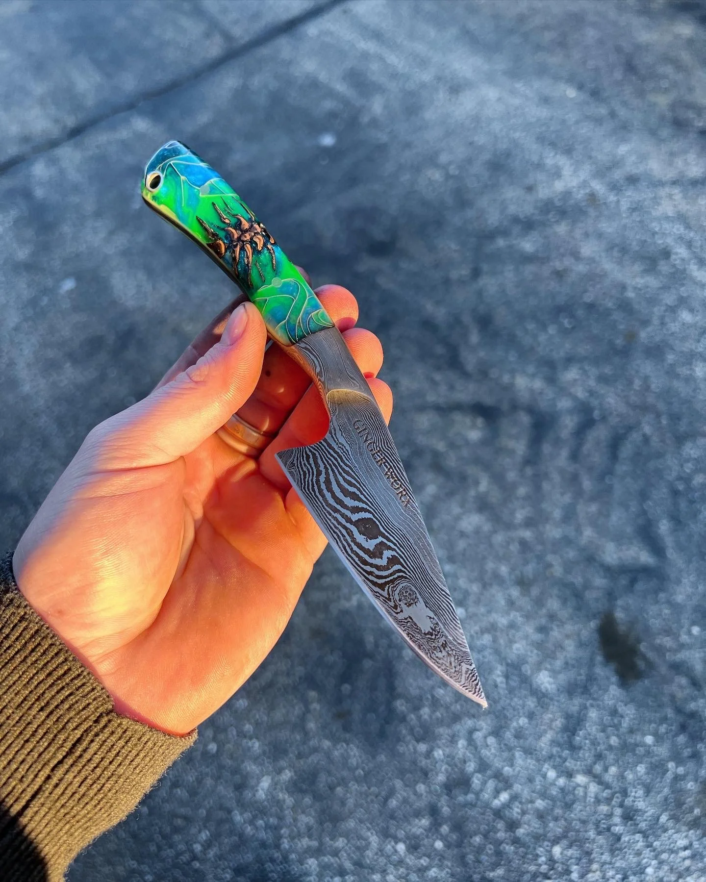 A hand holding a colorful fishing lure with a painted fish design and a patterned metal blade.