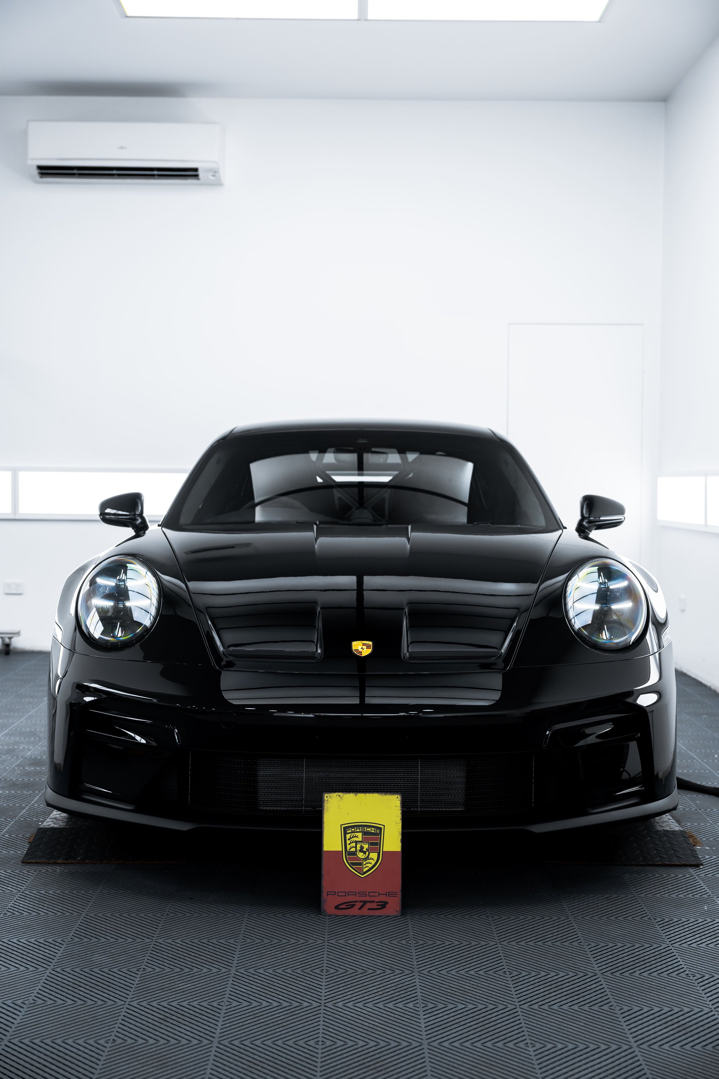 Front view of black Porsche 911 GT3 in detailing studio with headlights illuminated, showcasing flawless finish protected with PPF by ADS