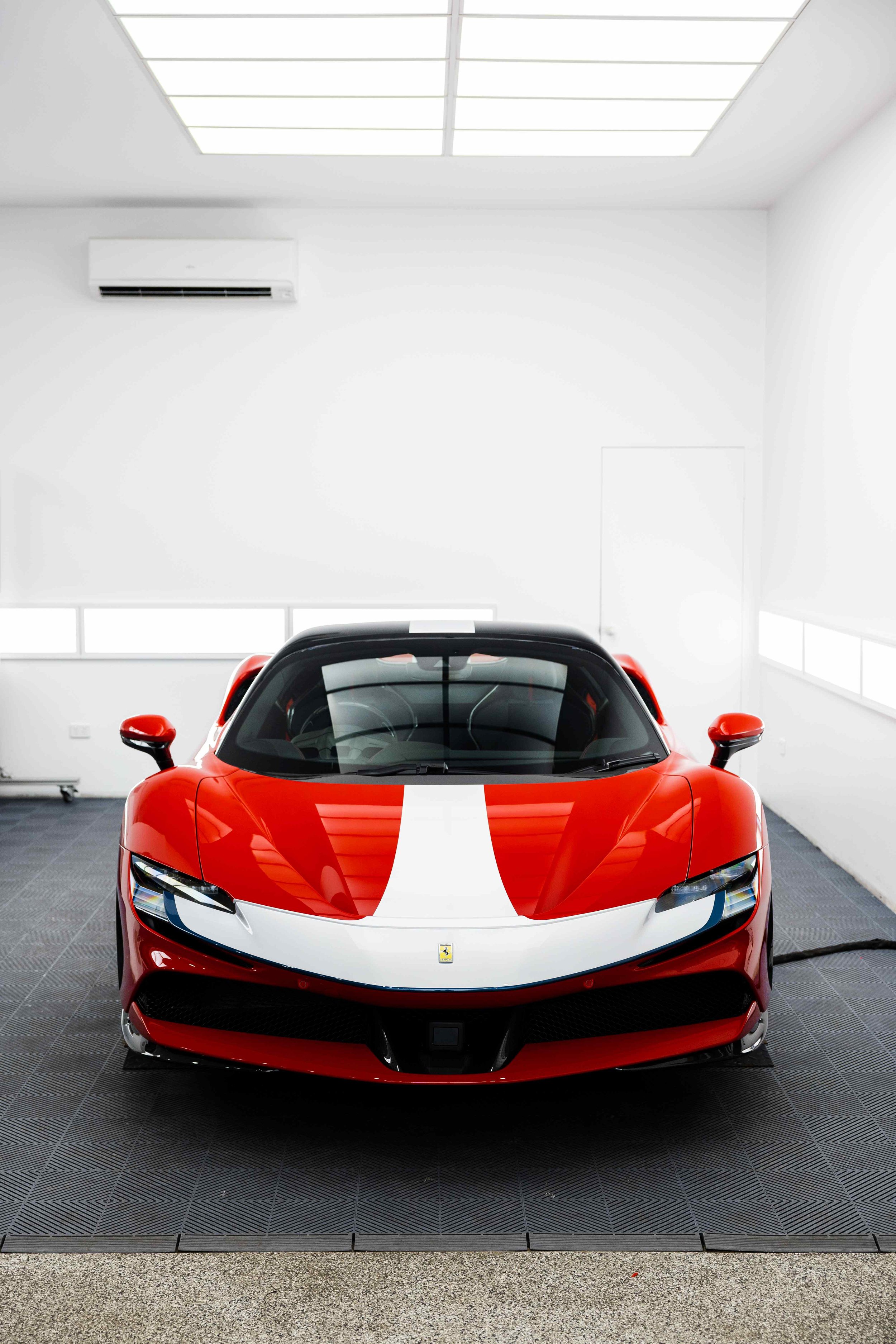 Red Ferrari SF90 Spyder front view in studio with white stripe and bonnet with XPEL Paint Protection Film in Mona Vale