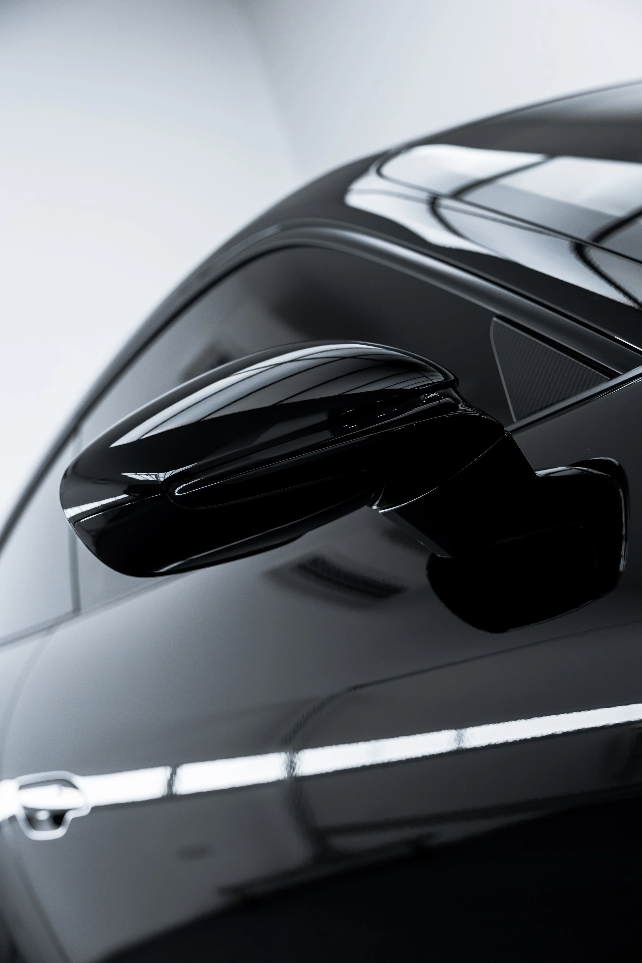 Close-up of black Porsche 911 GT3 side mirror with glossy finish reflecting studio lighting