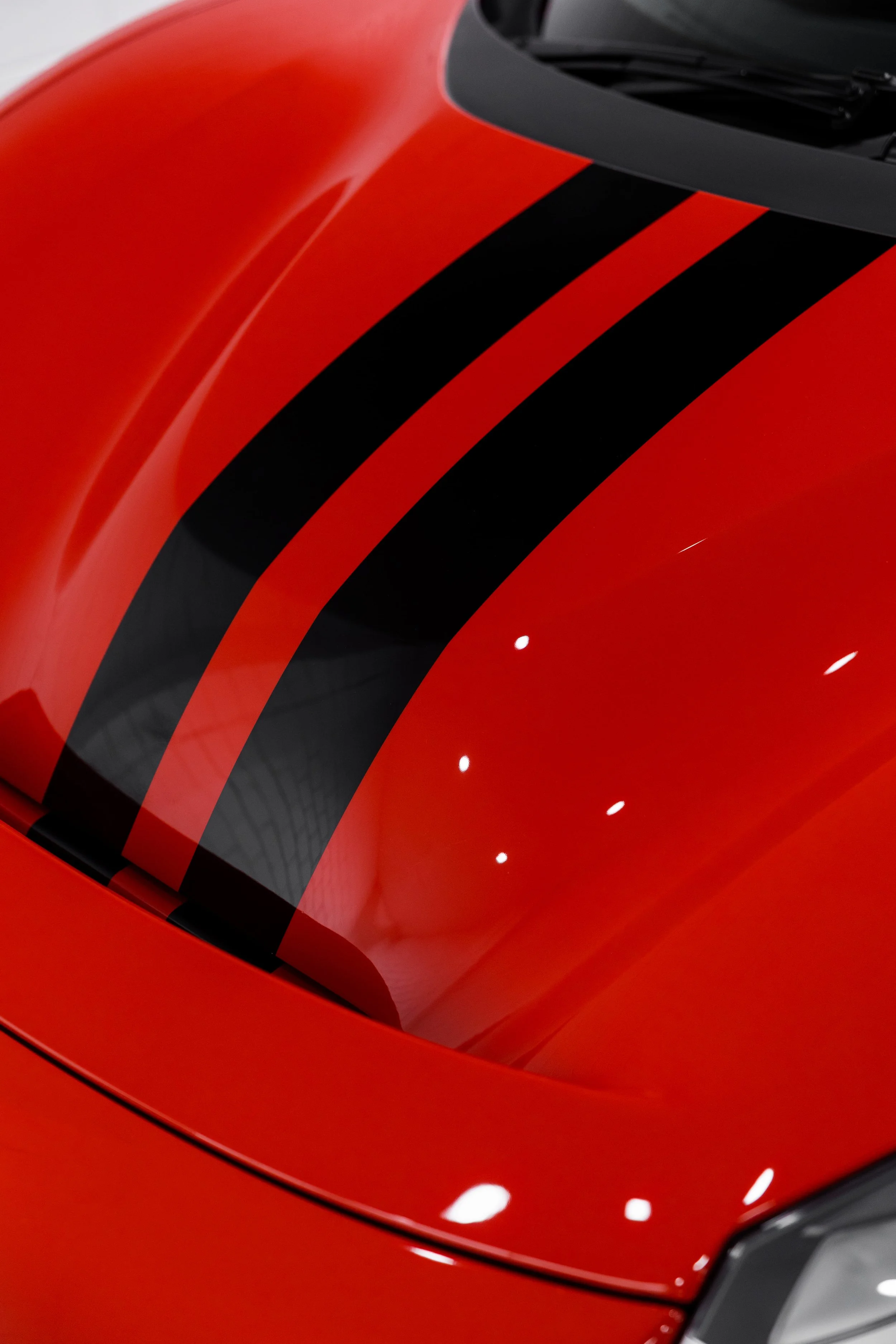 Close-up of Ferrari 488 Pista hood with black racing stripes over gloss red paint reflecting studio lighting