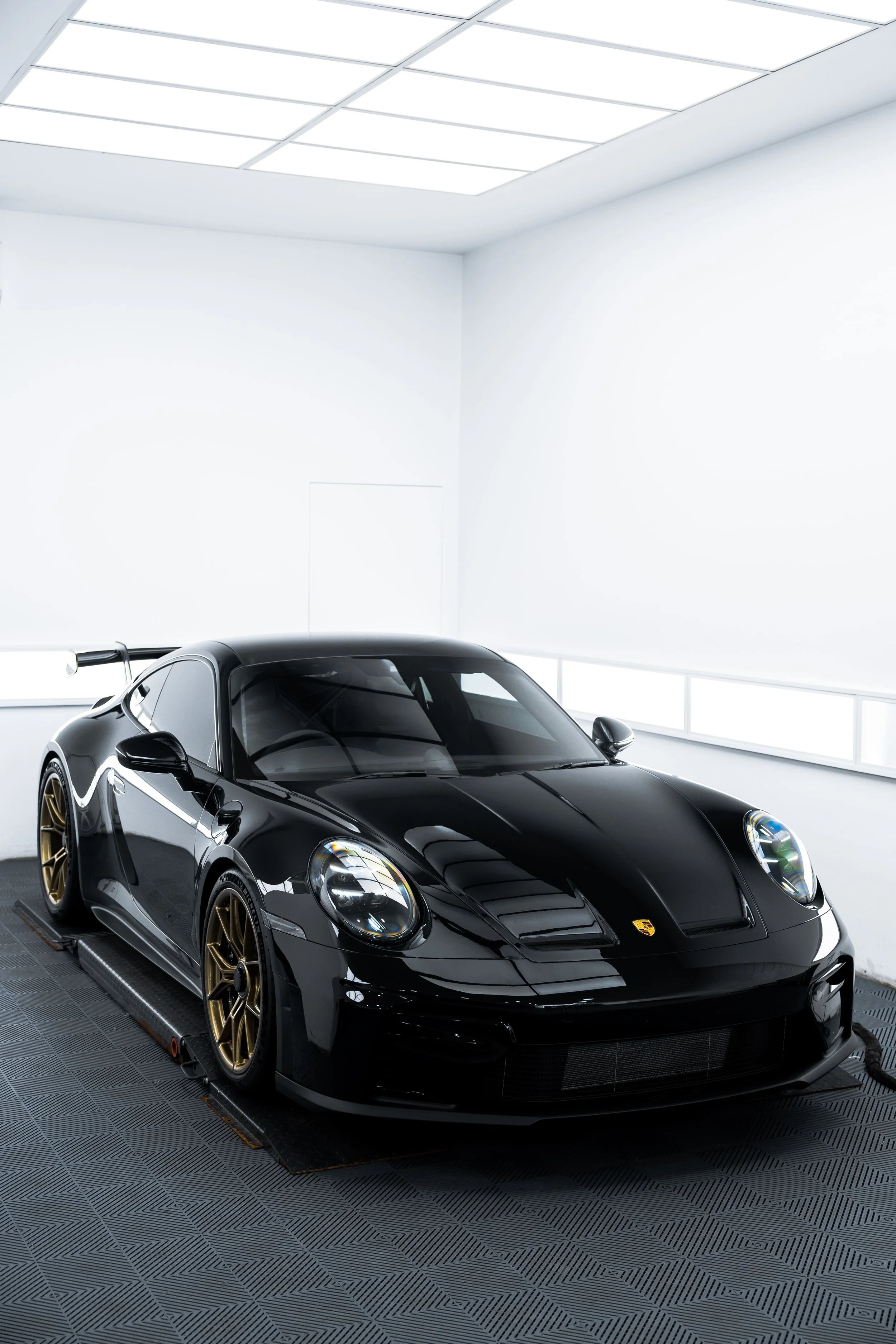 Front three-quarter view of black Porsche 911 GT3 with gold wheels inside a clean detailing studio