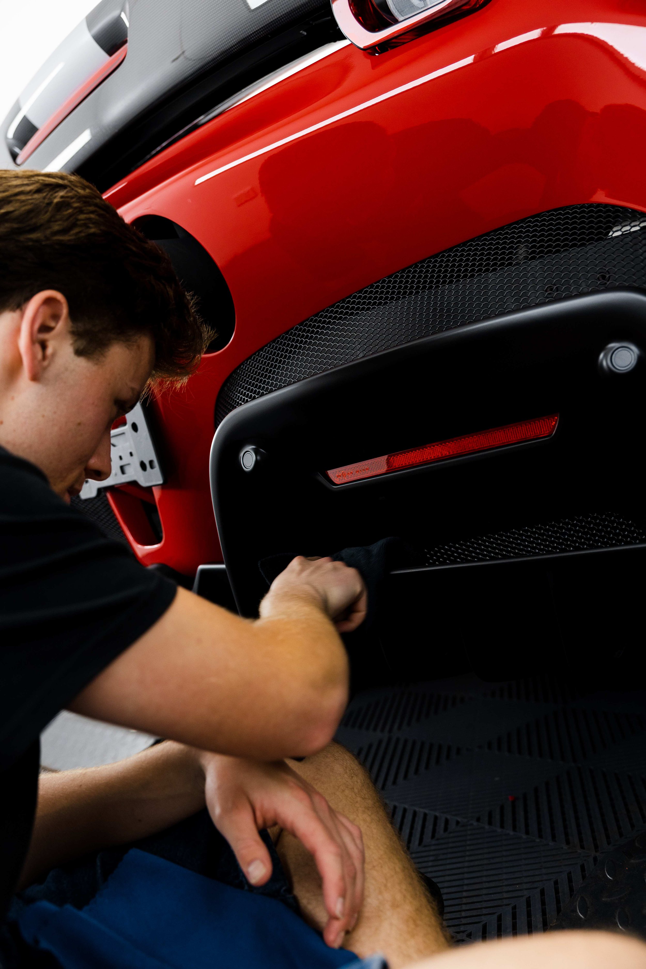 ADS technician working on the rear diffuser of a red Ferrari SF90 Spyder in Mona Vale