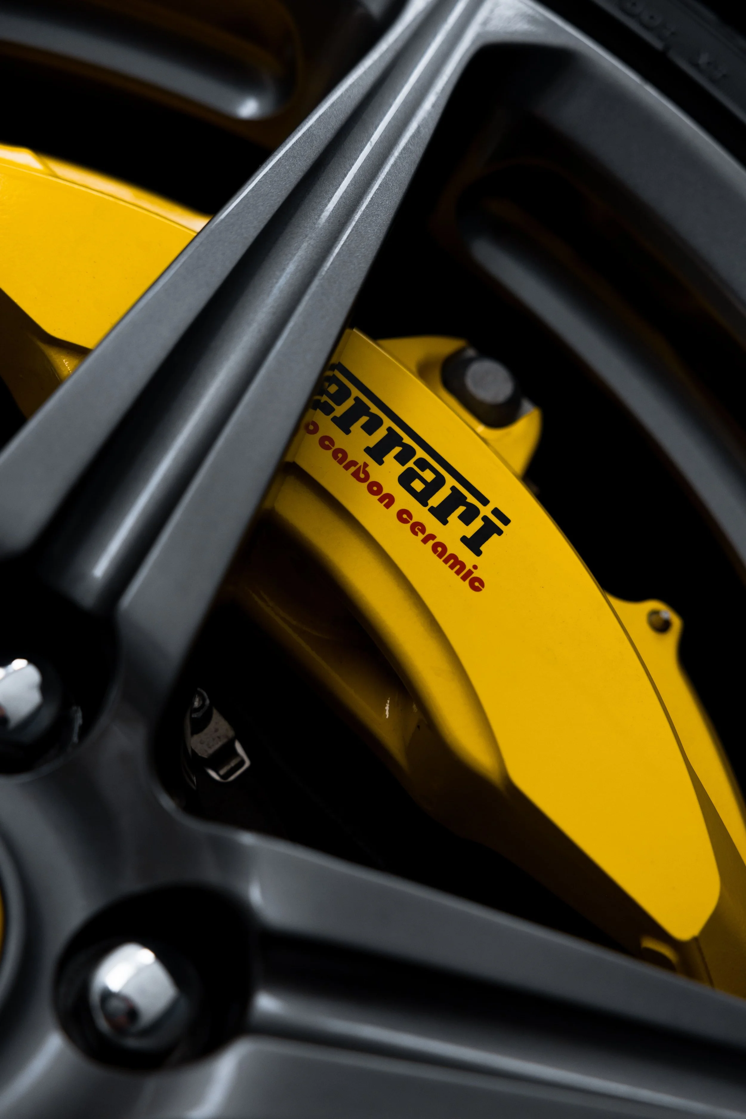 Close-up of Ferrari 458 wheel with yellow Ferrari carbon ceramic brake caliper behind black alloy rim, detailed and protected with PPF by ADS