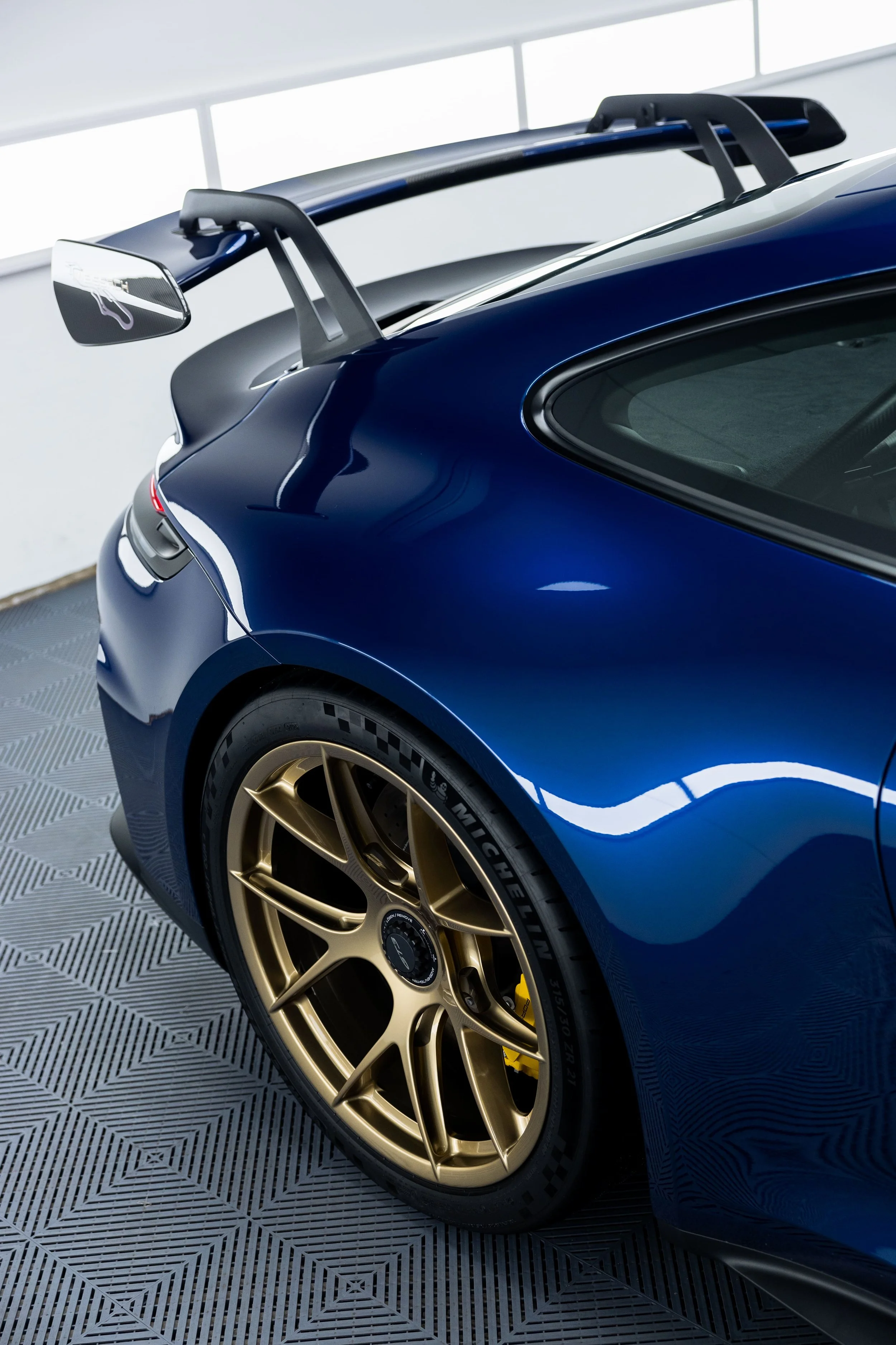 Rear quarter view of blue Porsche 911 GT3 with gold wheels and carbon rear wing inside a detailing studio