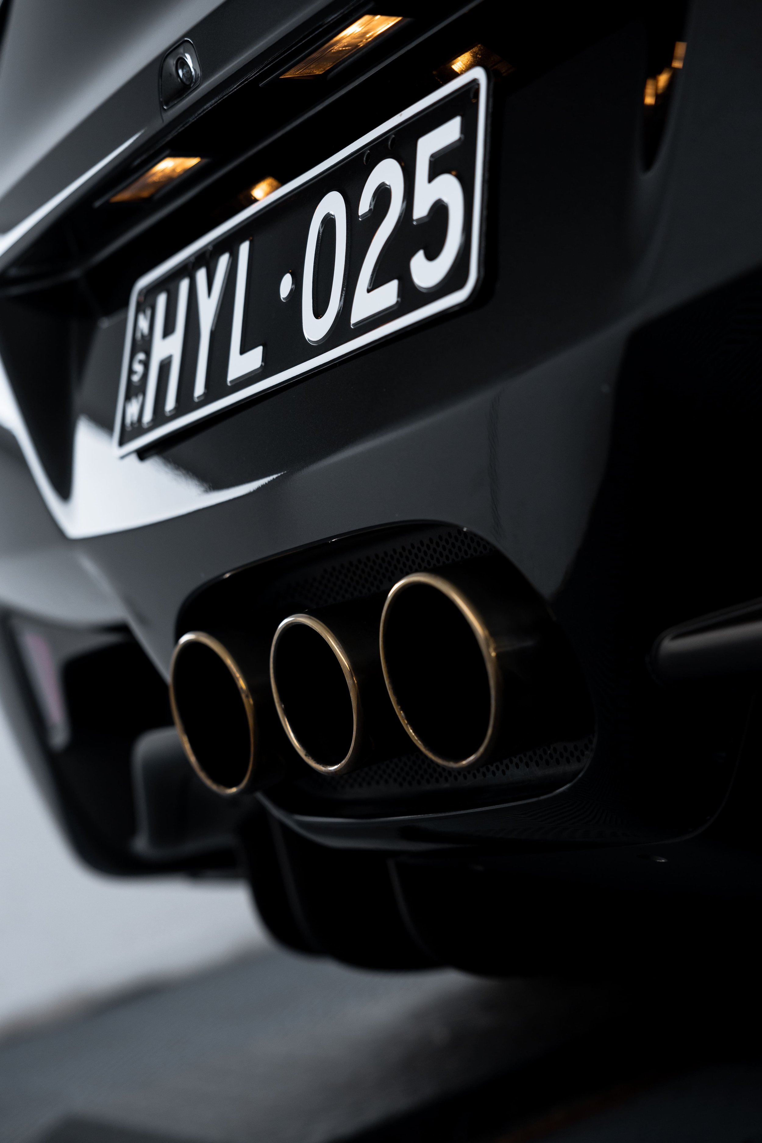Close-up of Ferrari 458 rear with NSW license plate HYL-025 and triple exhaust tips, detailed and protected with PPF by ADS