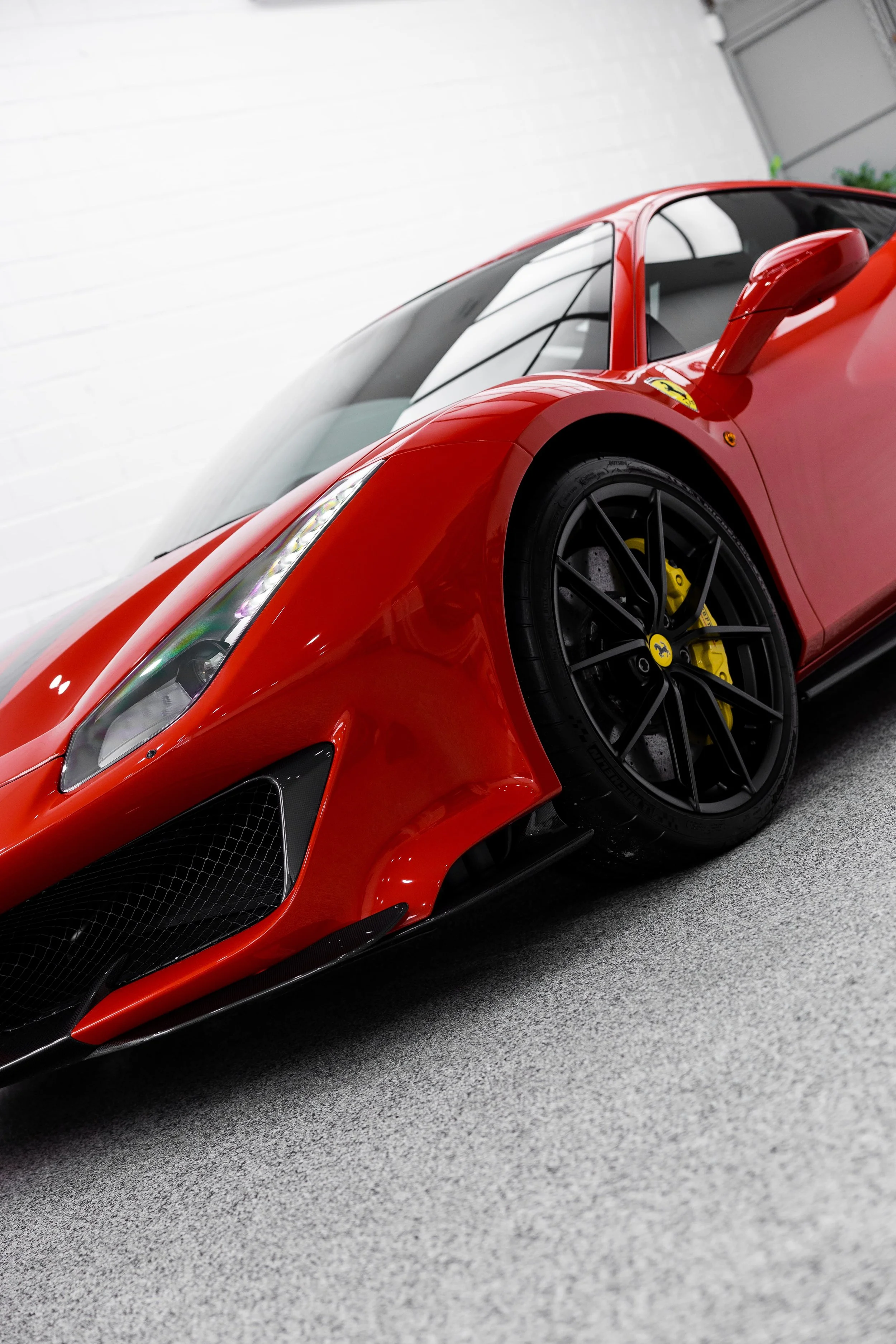 Front three-quarter view of Ferrari 488 Pista in red, highlighting aggressive stance, black wheels, and yellow brake calipers in studio