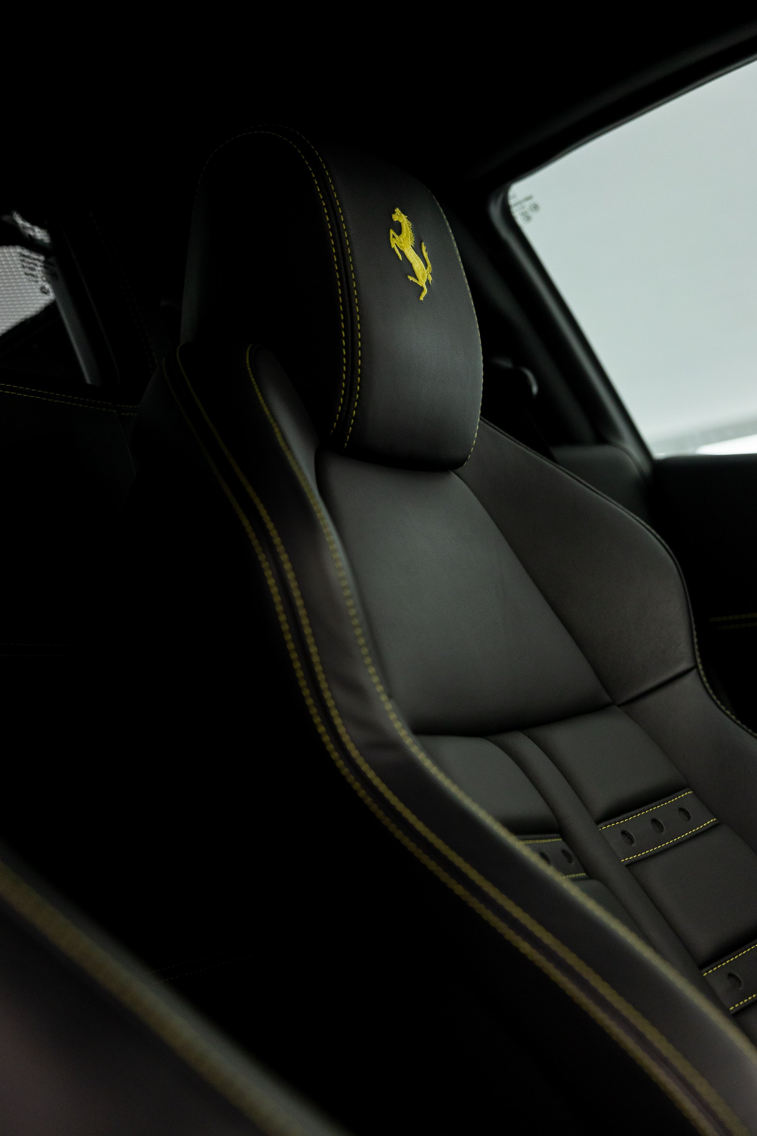Close-up of Ferrari 458 interior seat with yellow prancing horse emblem and contrast stitching, showcasing premium detailing by ADS