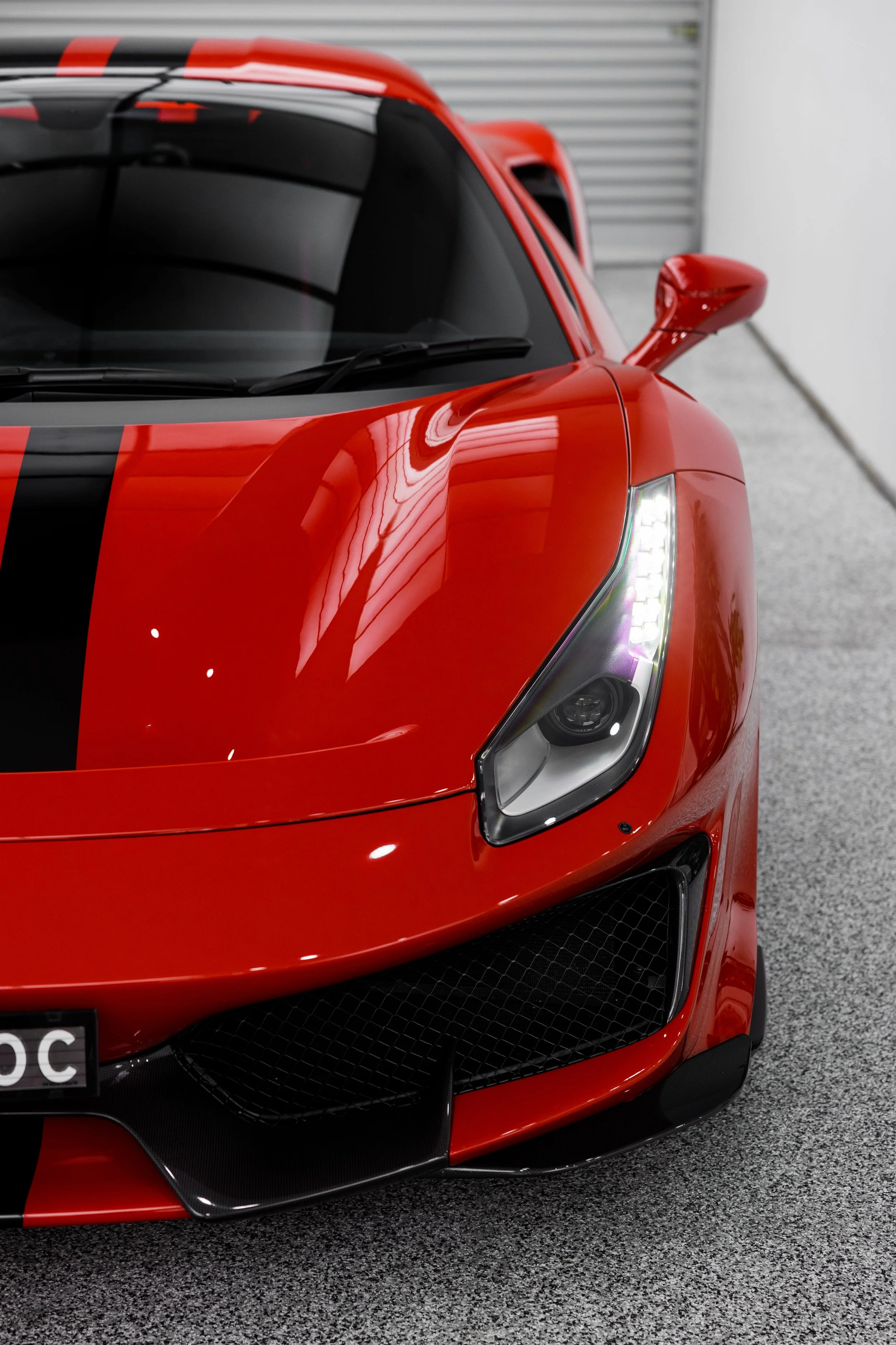 Close-up of Ferrari 488 Pista front end showing LED headlight, black racing stripe, and carbon fibre lower grille in studio