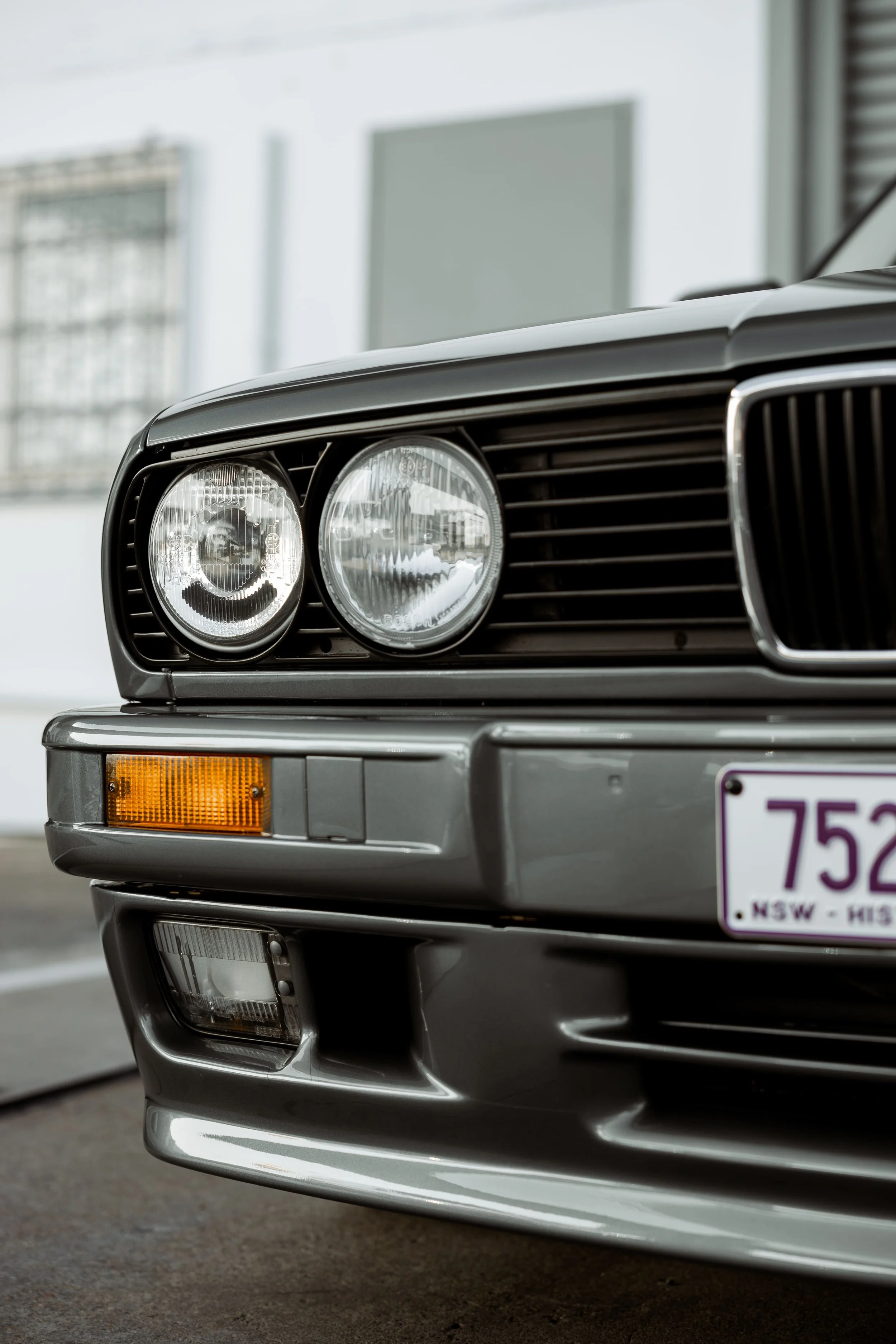 BMW E30 front end close-up showing dual round headlights, kidney grille and bumper detail, showcasing classic styling restored by Australian Detailing Services Sydney