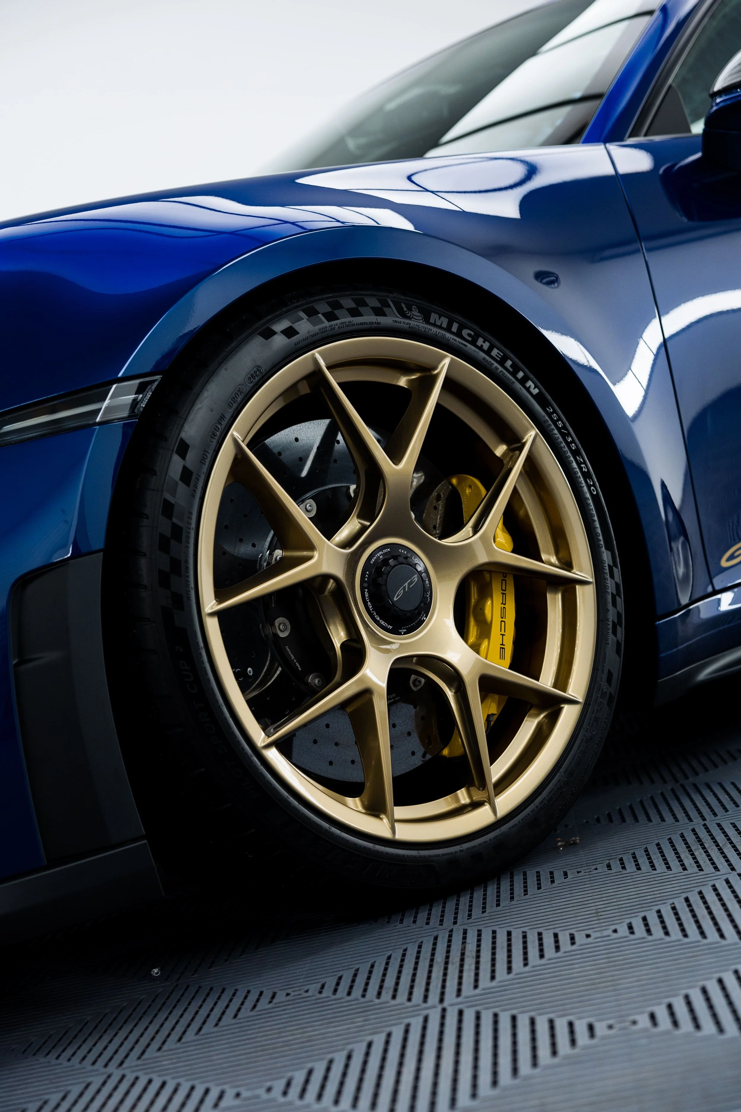 Close-up of blue Porsche 911 GT3 front wheel with gold centre-lock rim, carbon ceramic brake and Michelin tyre in detailing studio