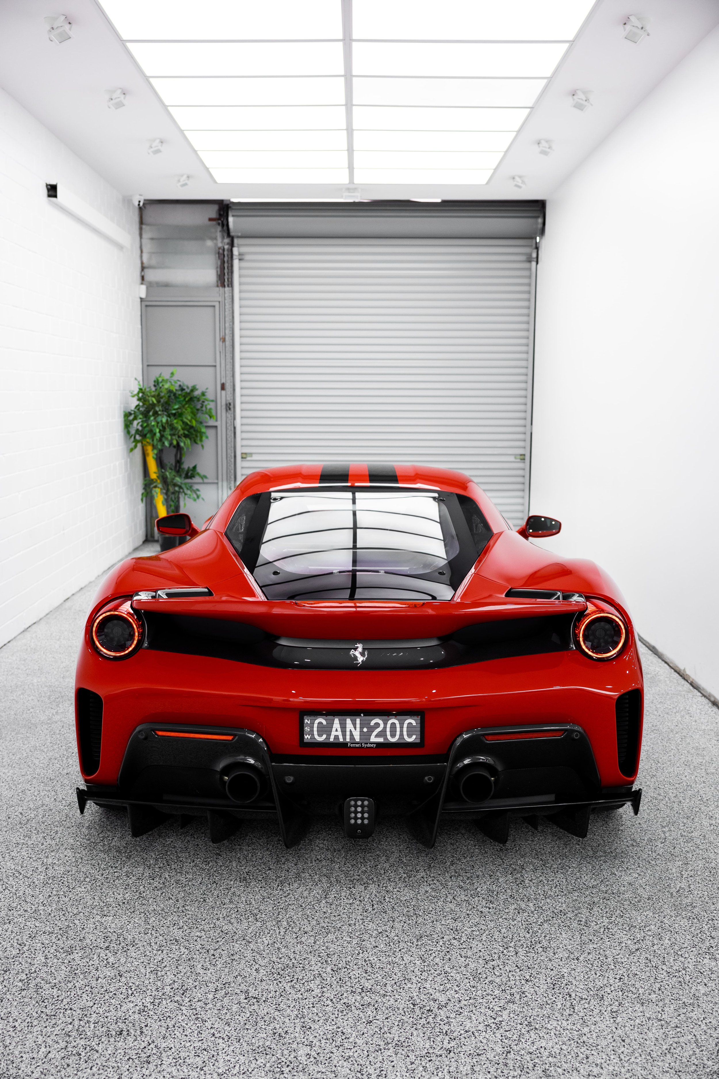 Rear view of Ferrari 488 Pista in red inside detailing studio, showcasing diffuser, dual exhausts, and LED taillights