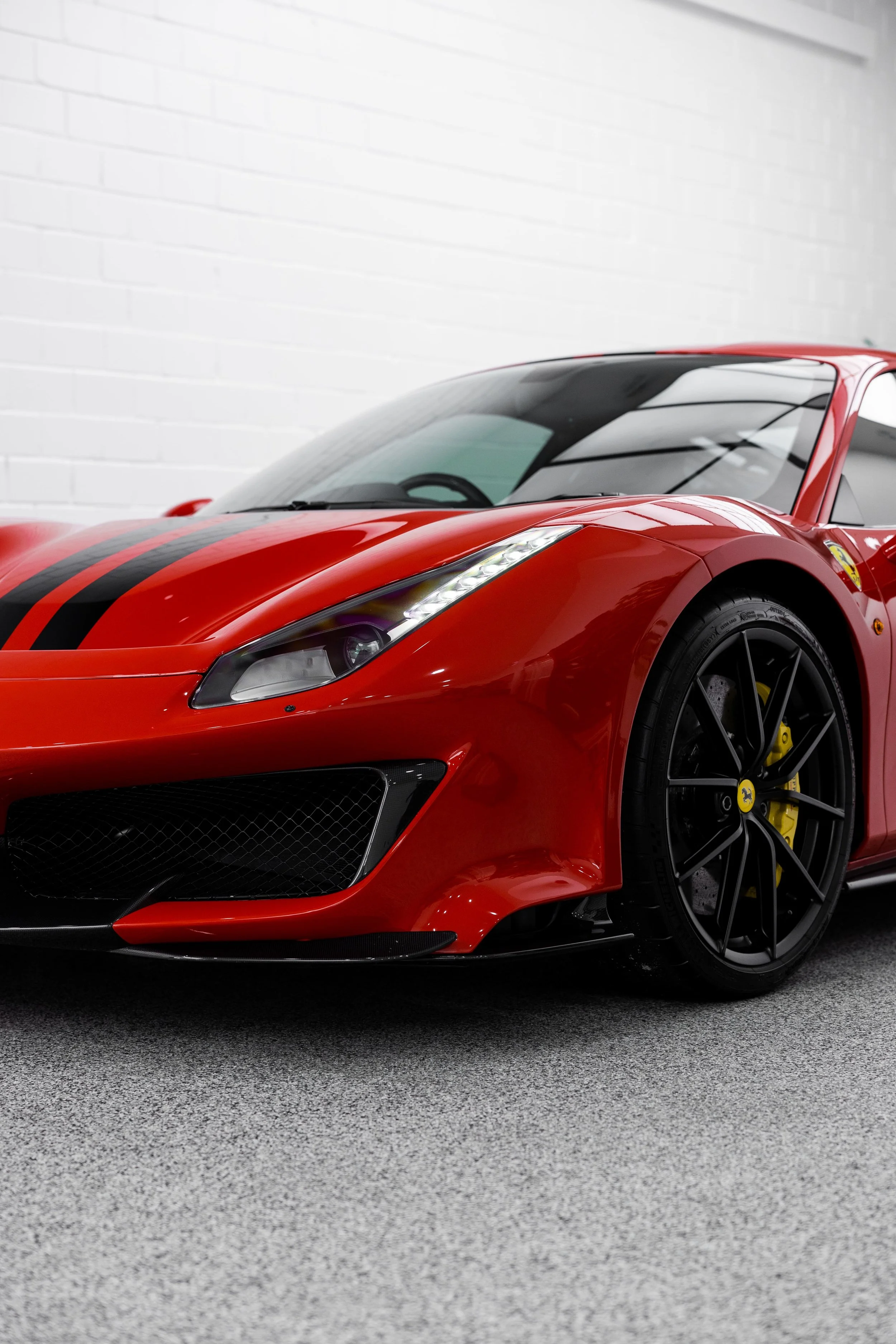 Front three-quarter view of Ferrari 488 Pista in red with black racing stripes, showcasing aggressive front bumper, LED headlights, and black alloy wheels