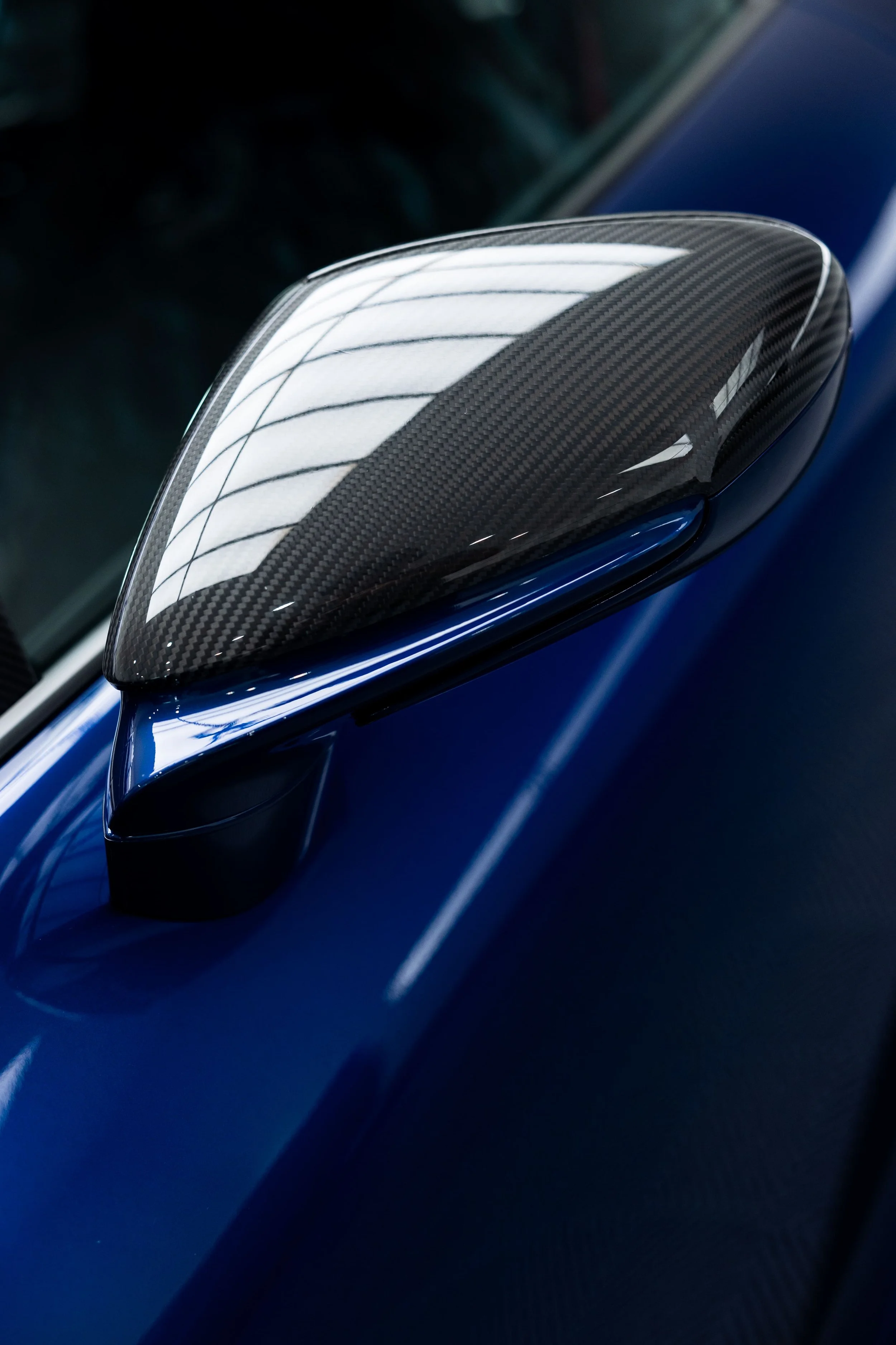 Close-up of blue Porsche 911 GT3 carbon fibre side mirror with glossy weave reflecting studio lighting