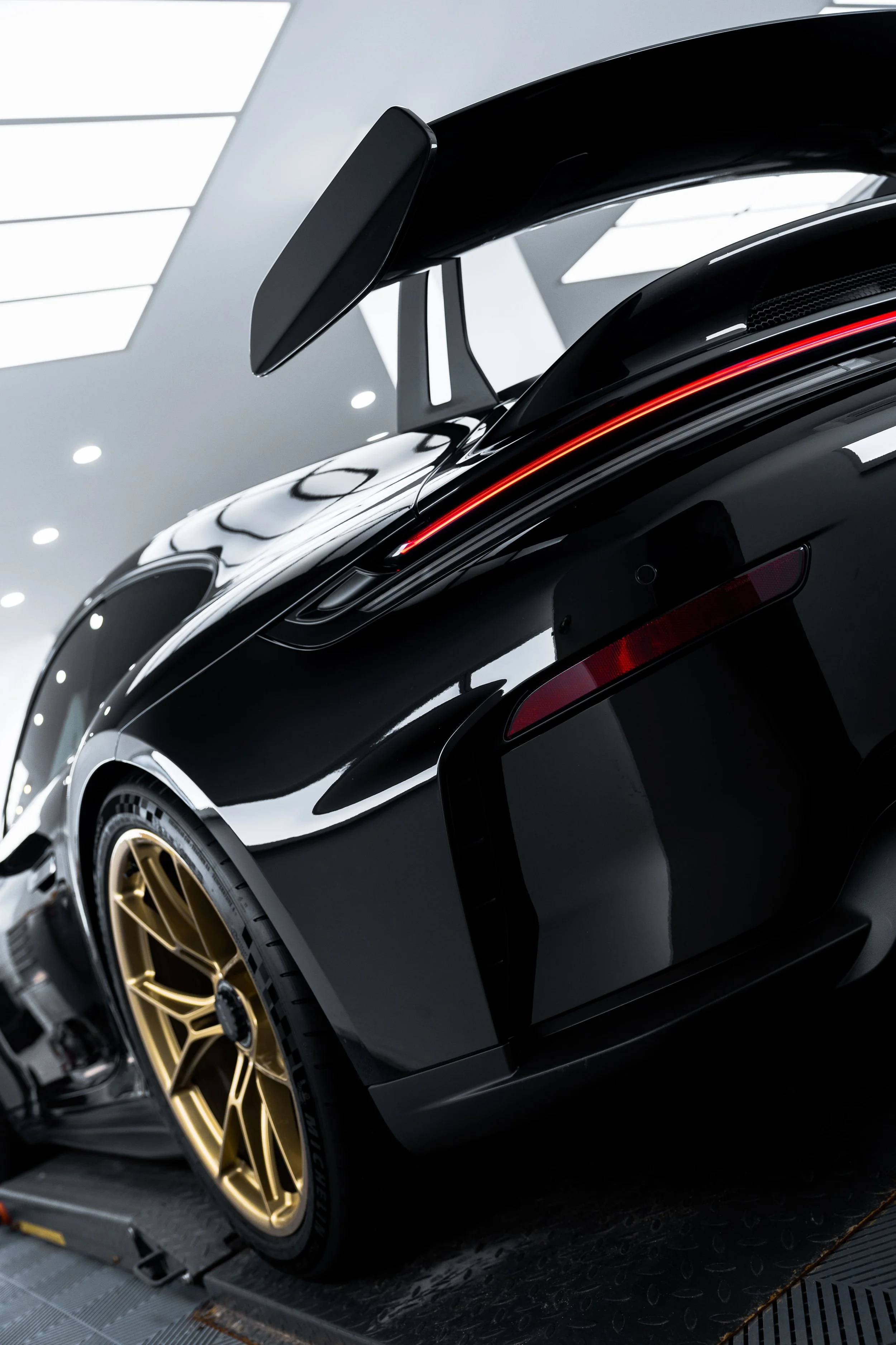 Rear three-quarter view of Porsche 911 GT3 with carbon wing, LED light bar, and gold wheels, showcasing high-gloss finish protected with PPF by ADS