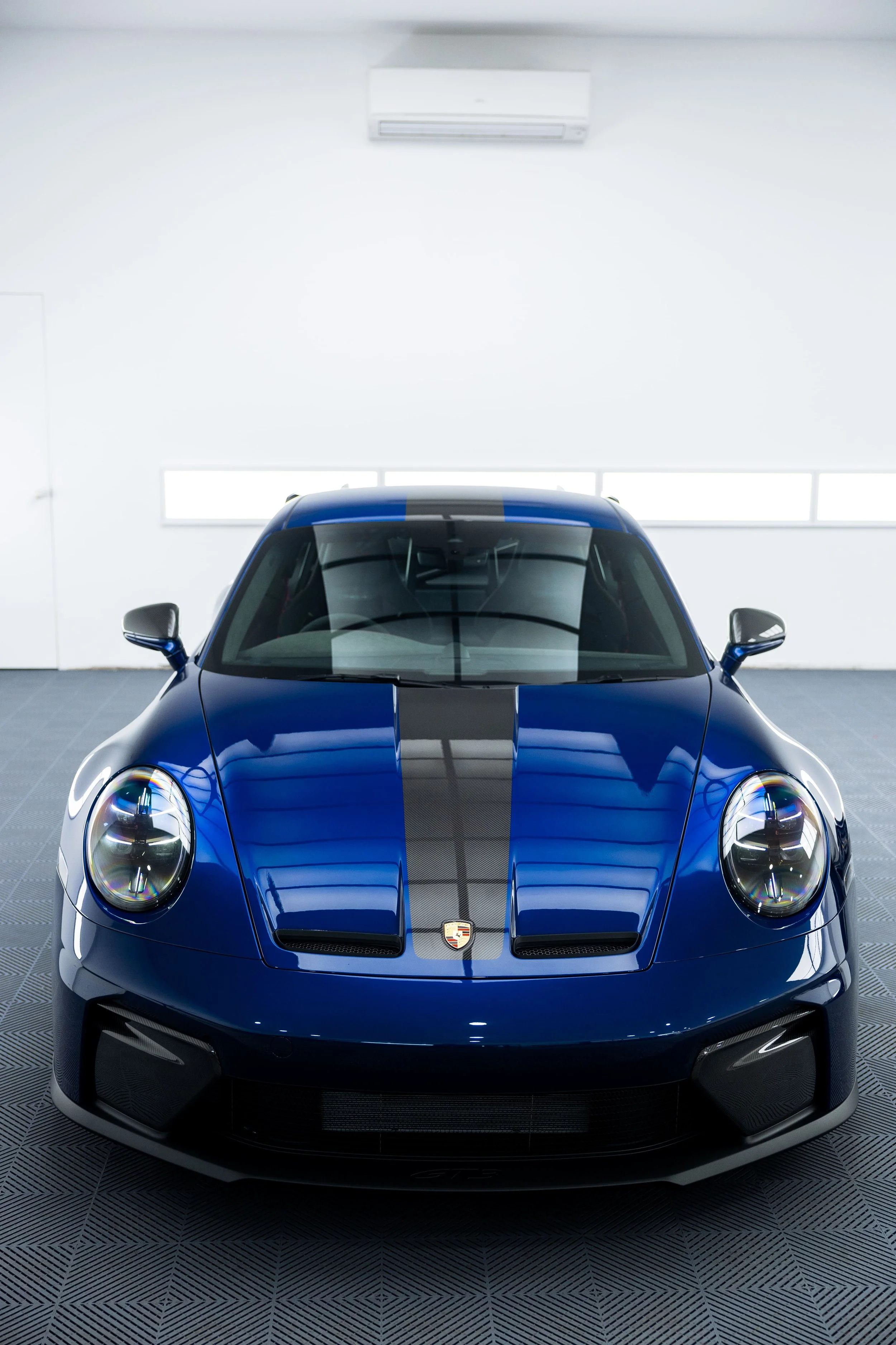 Front view of blue Porsche 911 GT3 with centre stripe inside a detailing studio, showcasing clean finish and PPF protection