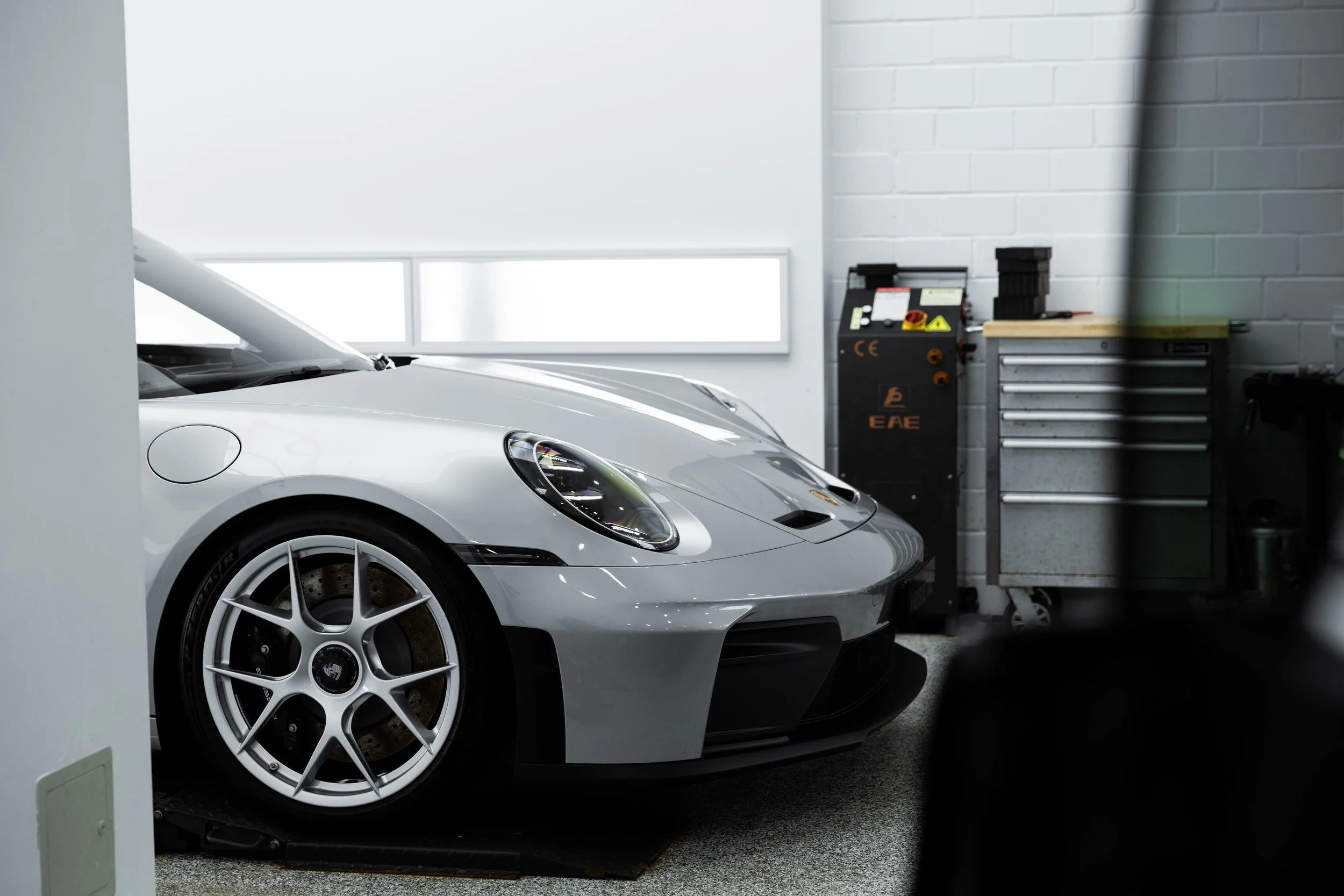 Silver Porsche 911 GT3 Touring front quarter view highlighting wheel, headlight and sculpted bumper inside workshop, finished with premium protection by Australian Detailing Services Sydney