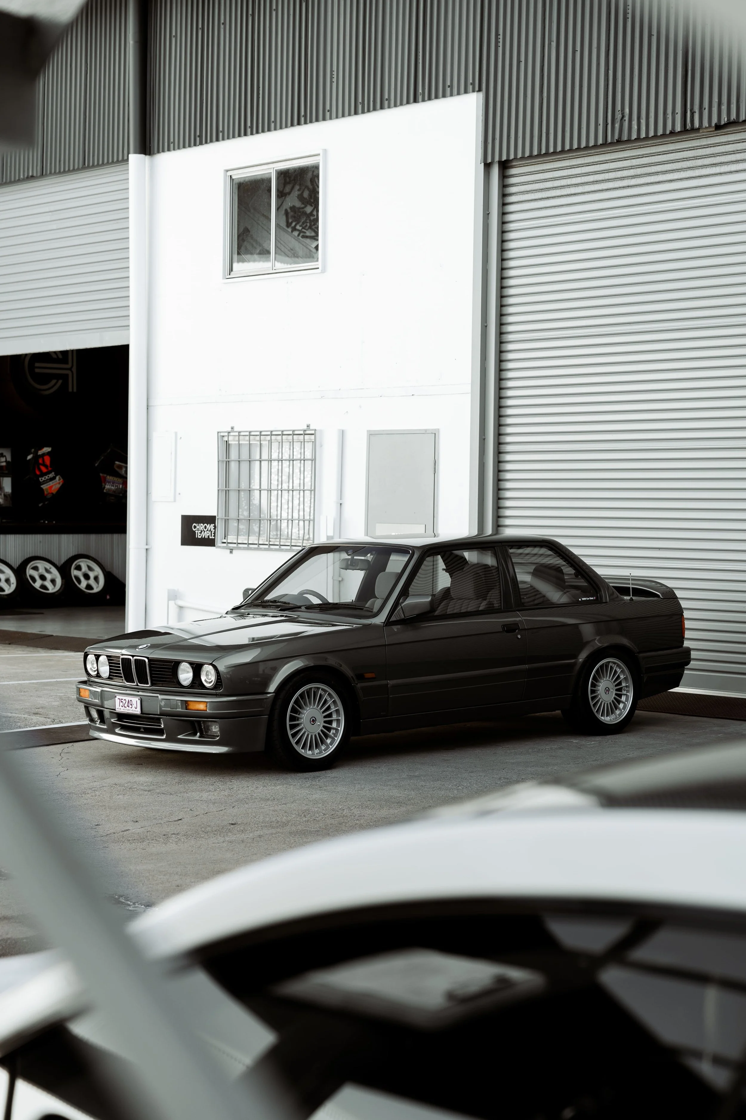 BMW E30 parked outside industrial workshop, showcasing classic boxy silhouette and timeless design, detailed and protected by Australian Detailing Services Sydney