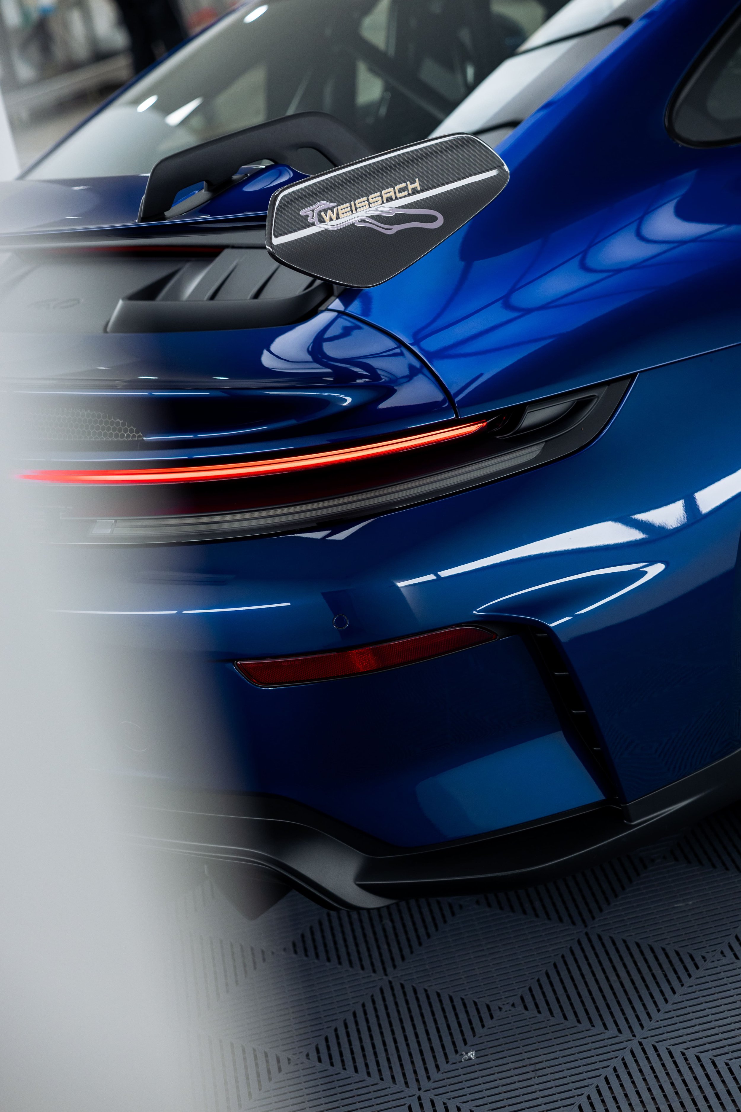 Rear quarter view of blue Porsche 911 GT3 with Weissach package wing and illuminated LED tail light inside detailing studio