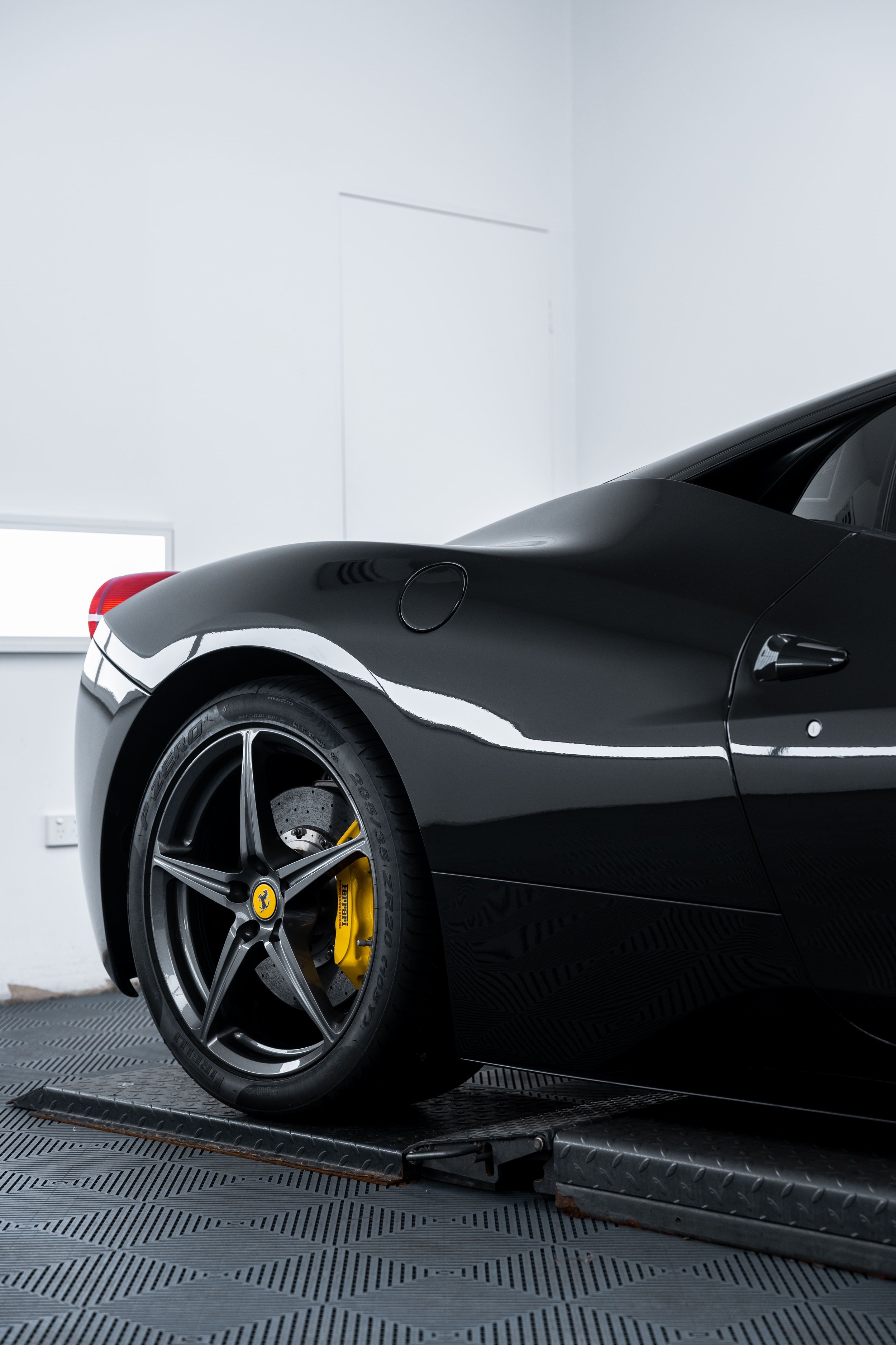 Side rear view of black Ferrari 458 with alloy wheel and yellow brake caliper, detailed and protected with PPF by ADS