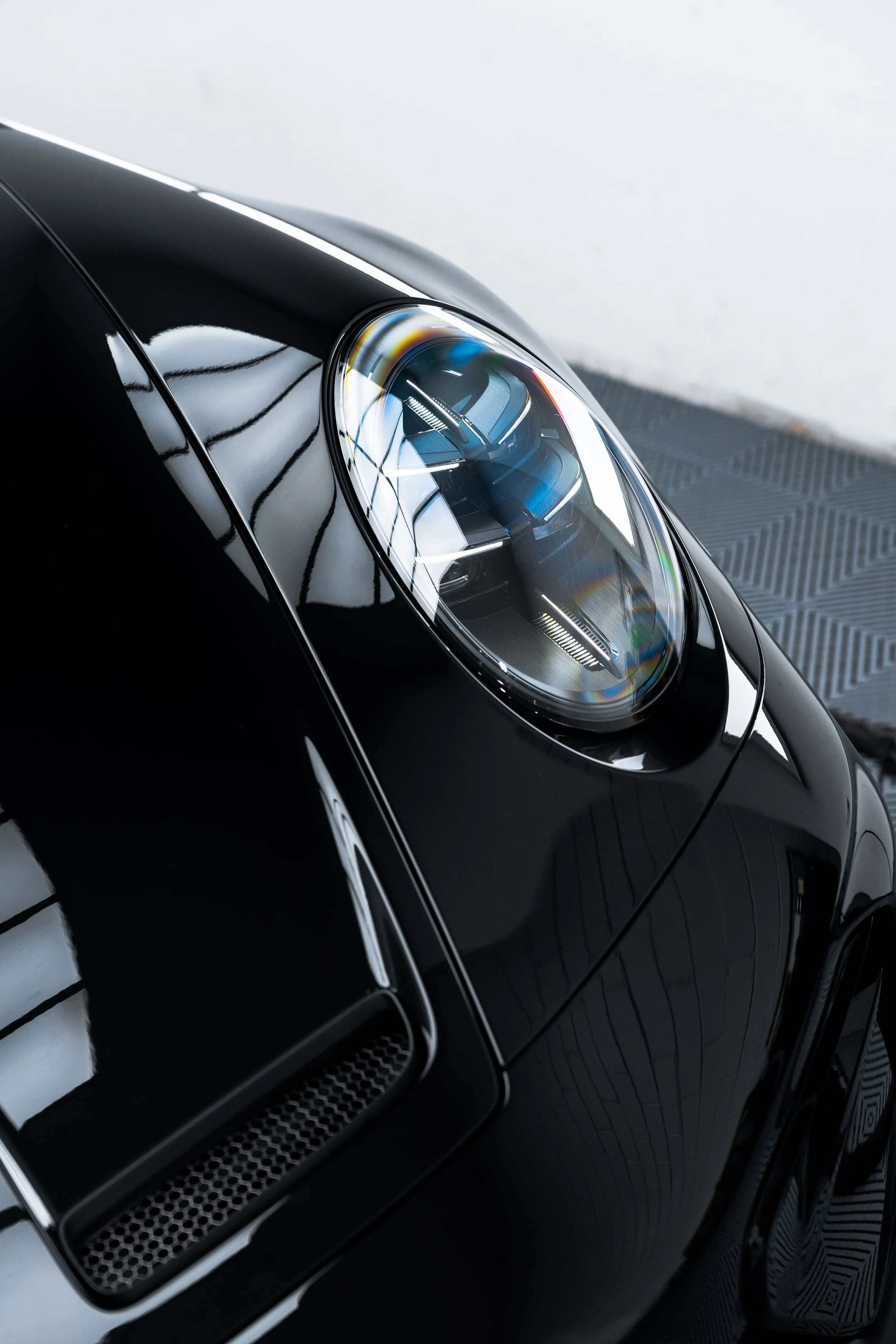 Close-up of Porsche 911 GT3 LED headlight and front fender with reflections in a detailing studio