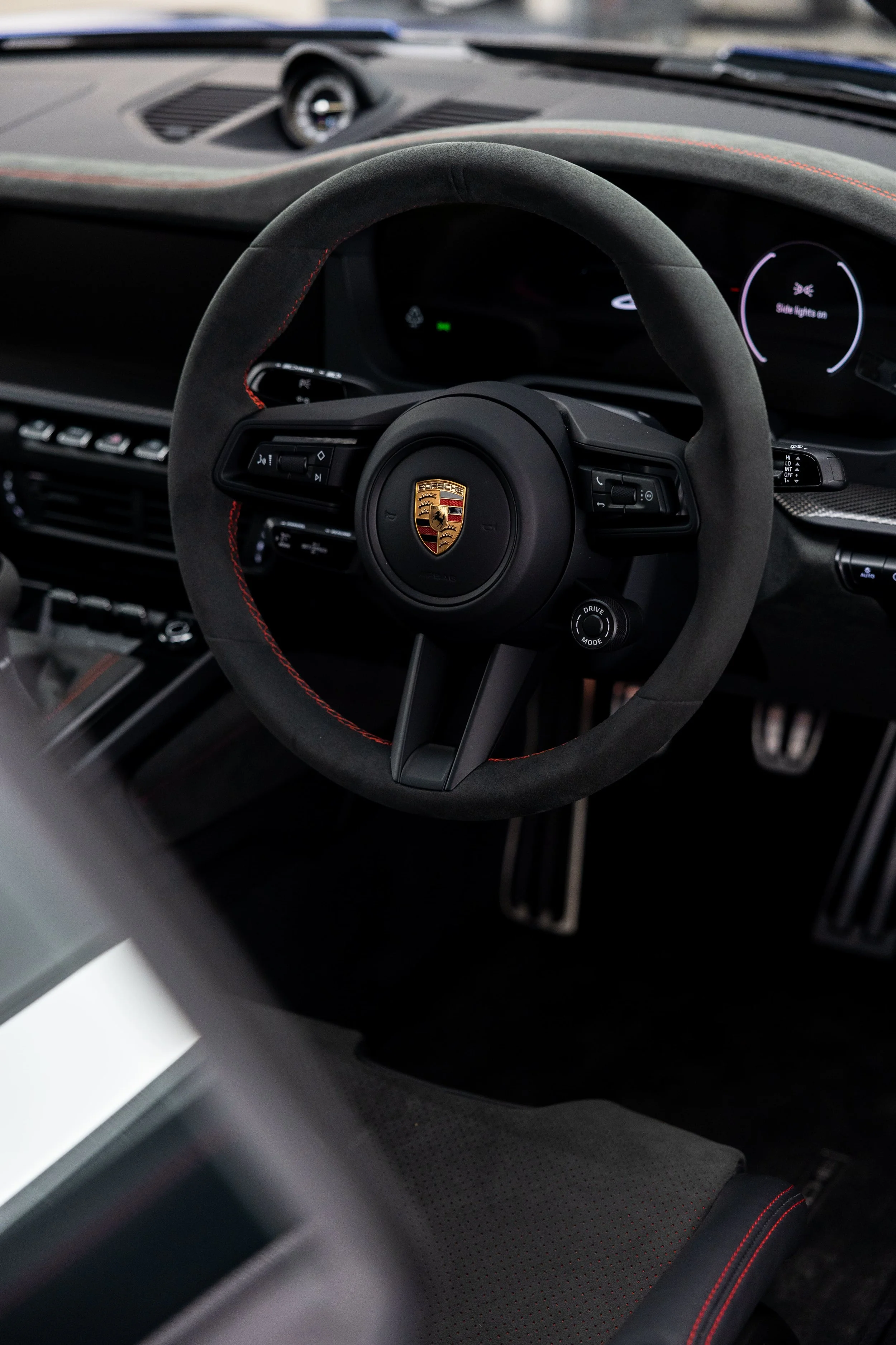 Interior view of Porsche 911 GT3 showing steering wheel with Porsche crest, digital display, and Alcantara finish with red stitching