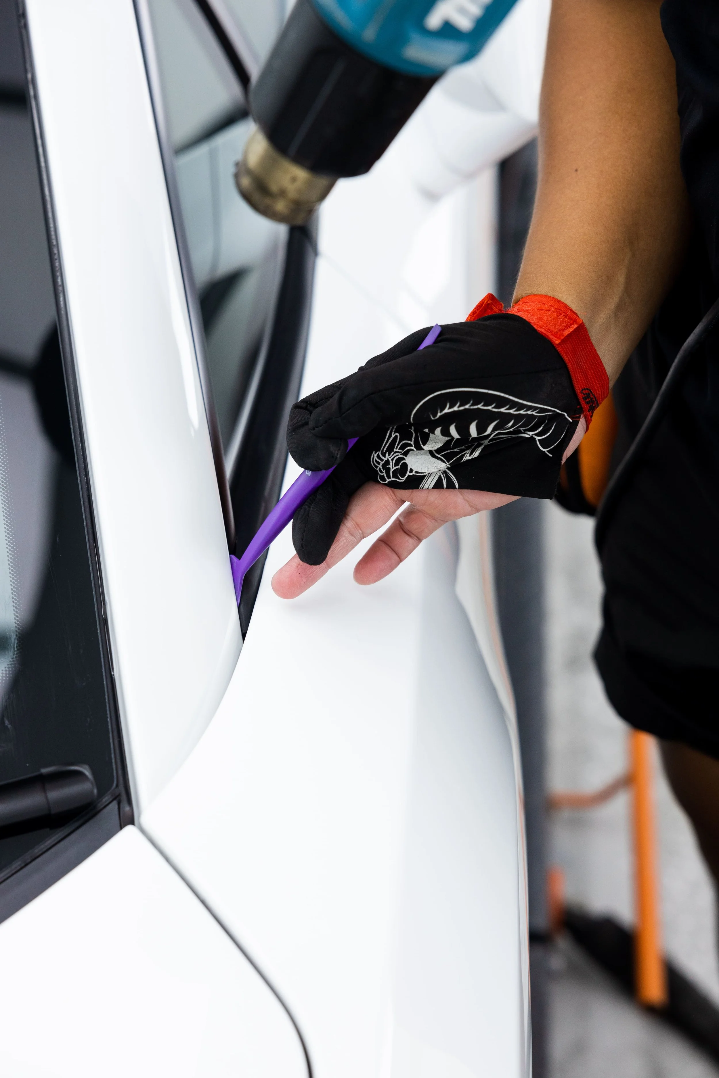 Detailer applying paint protection film to Lamborghini Gallardo panel using precision tool and heat gun
