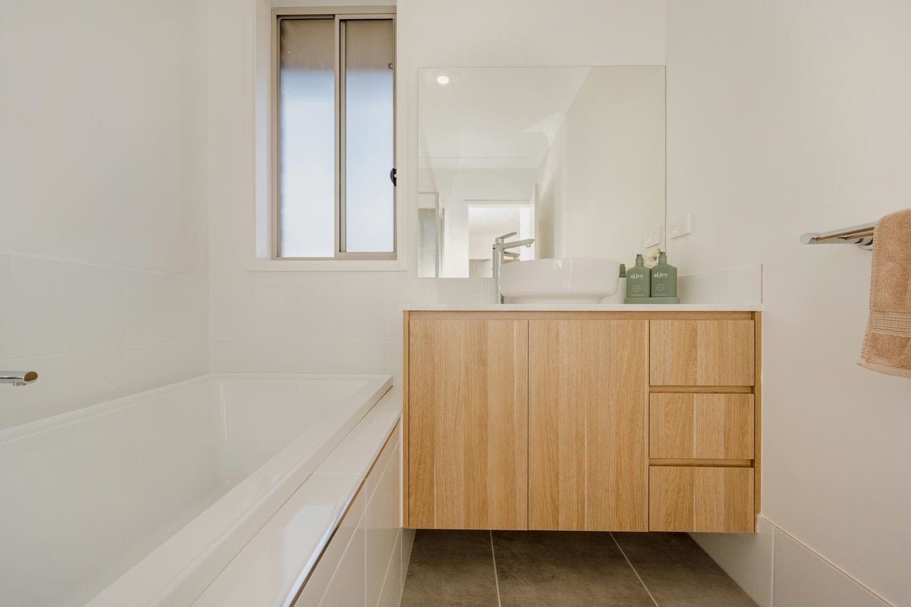 Bathroom with bath and light oak wooden vanity and white sink_Carnelian Projects.jpg