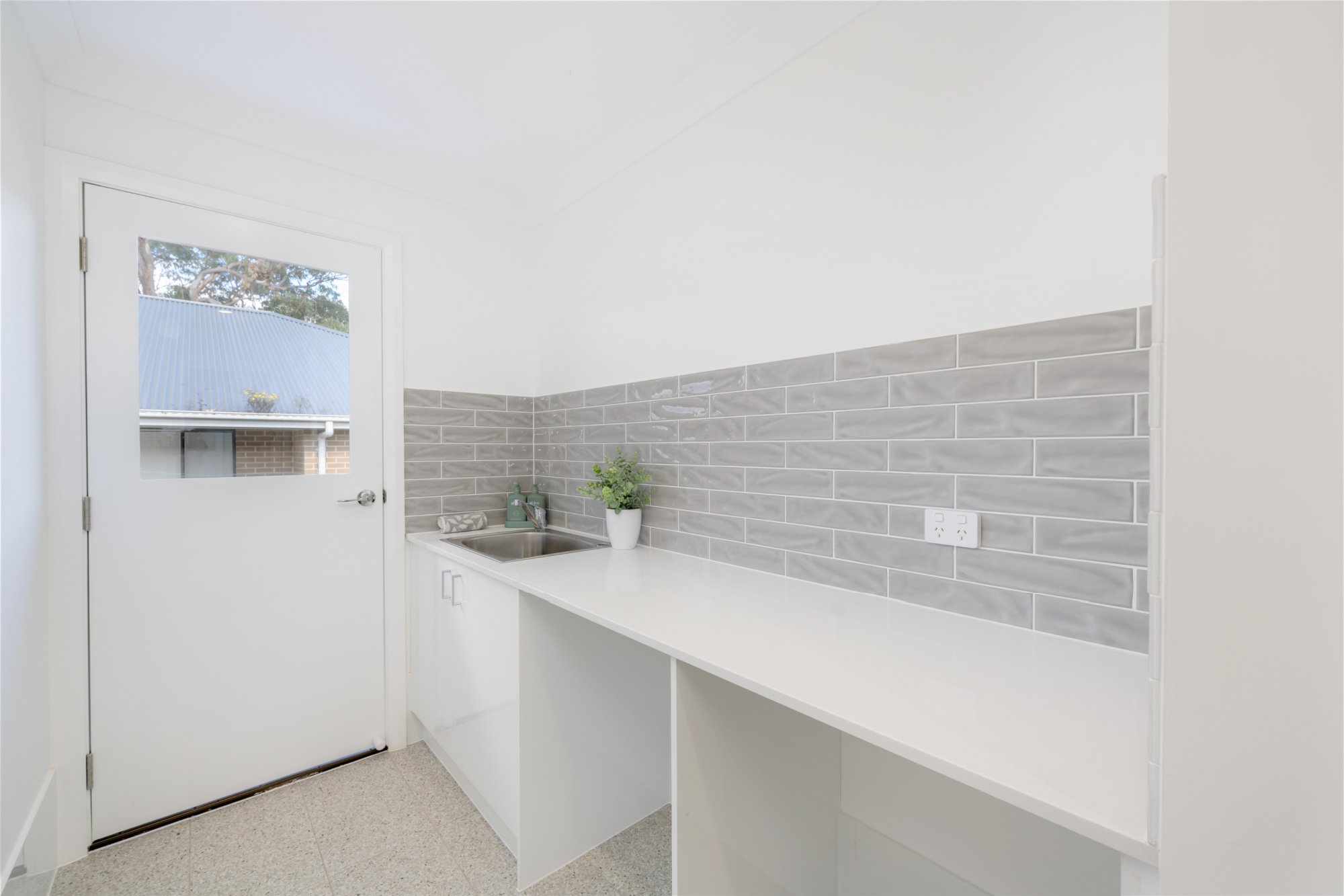 White laundry with light grey textured subway tile splashback, sink and external door with window_Carnelian Projects.jpg