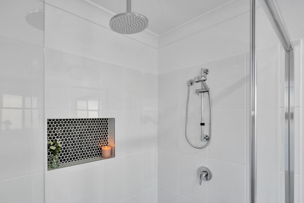 White bathroom shower with black mosaic tiles in niche, monsoon shower and hand held shower rail and chrome tap_Carnelian Projects.jpg