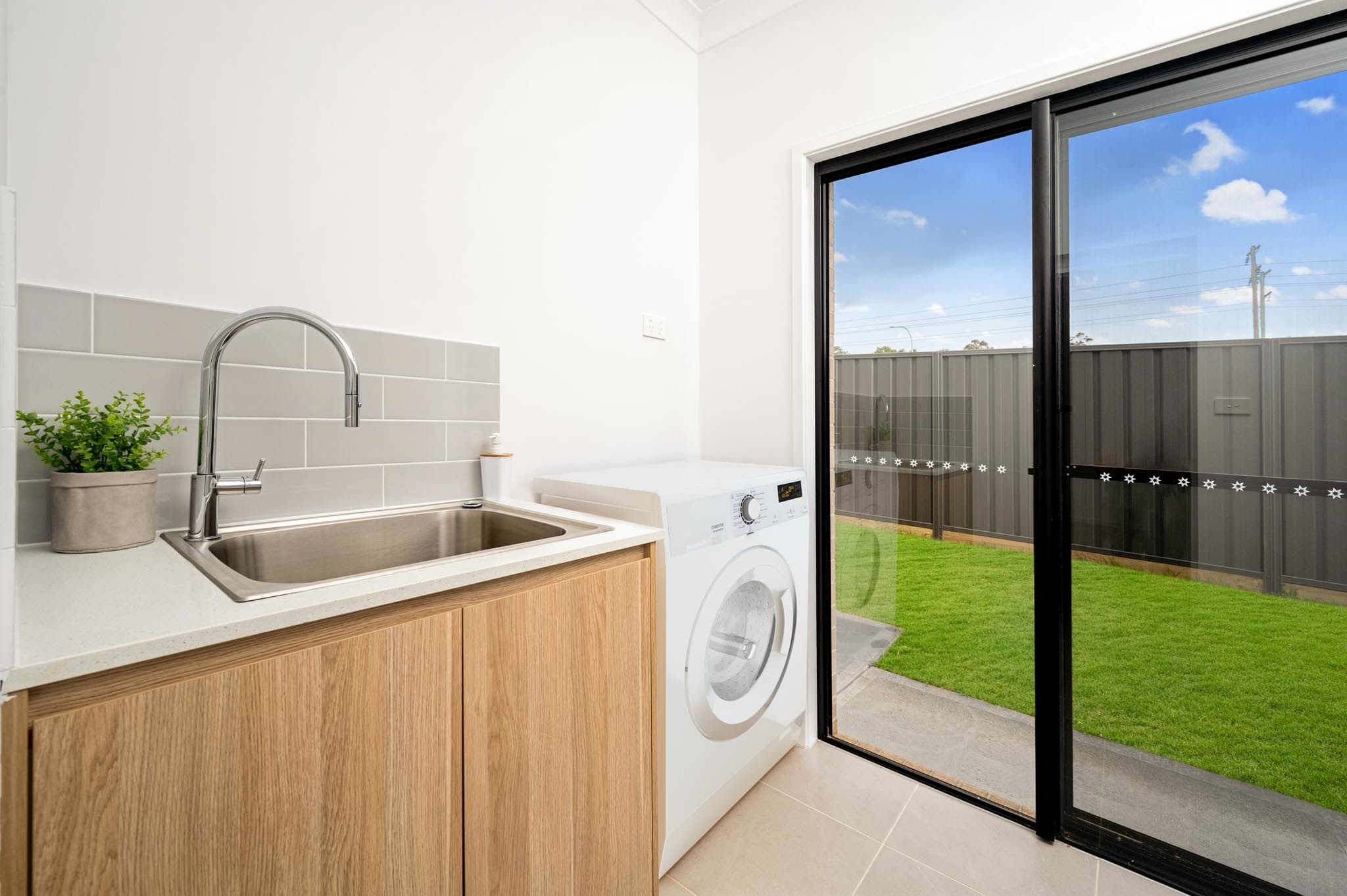 Laundry with light oak wooden cabinetry, grey subway tiles splashback, gooseneck chrome tap and sink with sliding external doors_Carnelian Projects.jpg