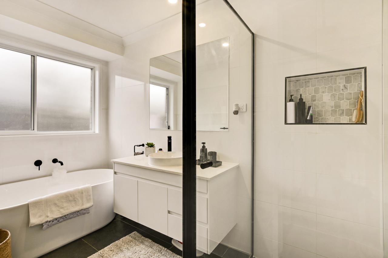 Main bathroom with white vanity, white tiles, black frame shower screen and grey tiled shower niche.jpg