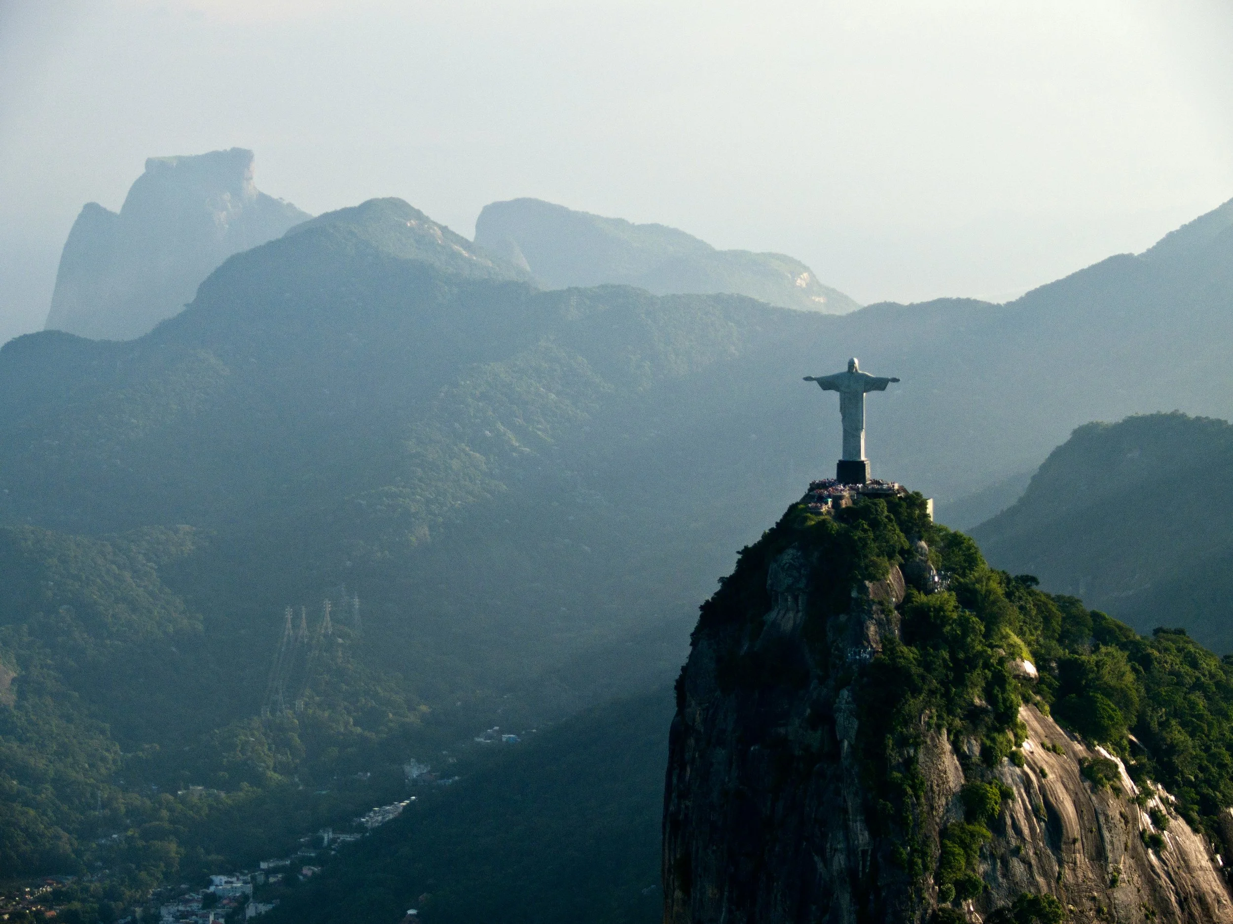 Christ the Redeemer statue on Corcovado Mountain in Rio de Janeiro, Brazil, with lush green hills and mountains in the background.