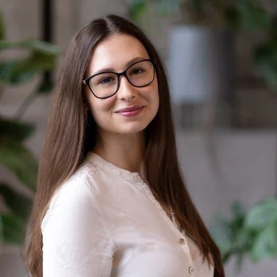 Photo of woman with long brown hair, a white shirt and black-framed glasses smiling
