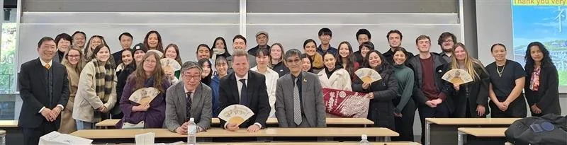 Group of students and instructors in a classroom, some holding fans and gifts, posing for a photo.