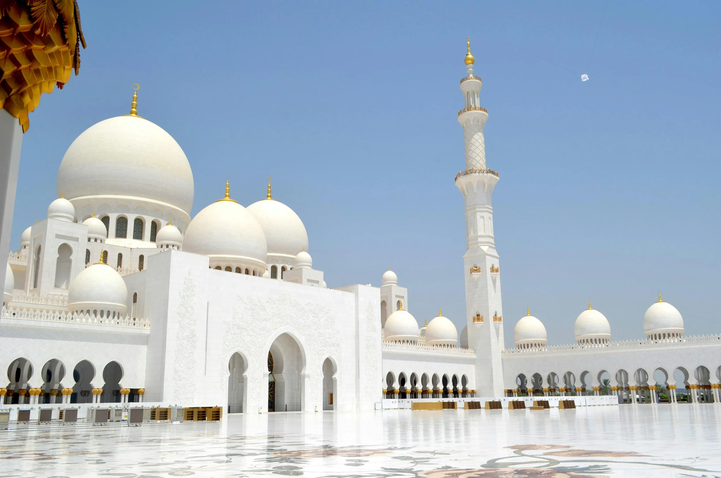 The Sultan Qaboos Grand Mosque in Muscat, Oman, with white domes, minaret, and intricate architecture under a clear blue sky.