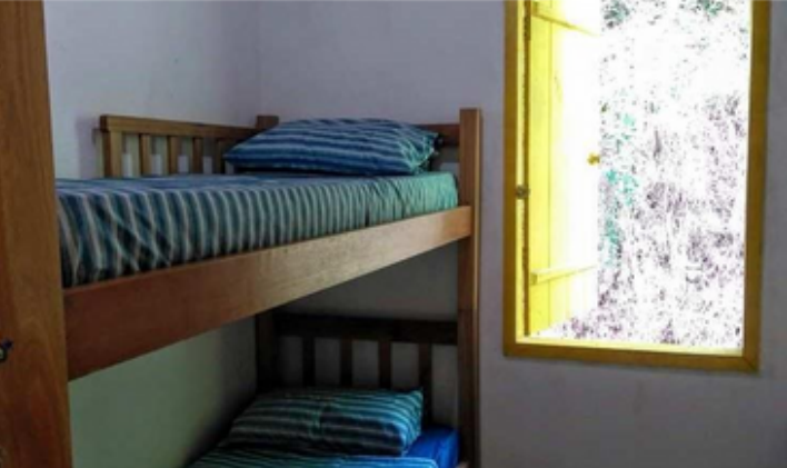 Bunk bed with striped mattresses and pillows next to a yellow window with visible outside trees.