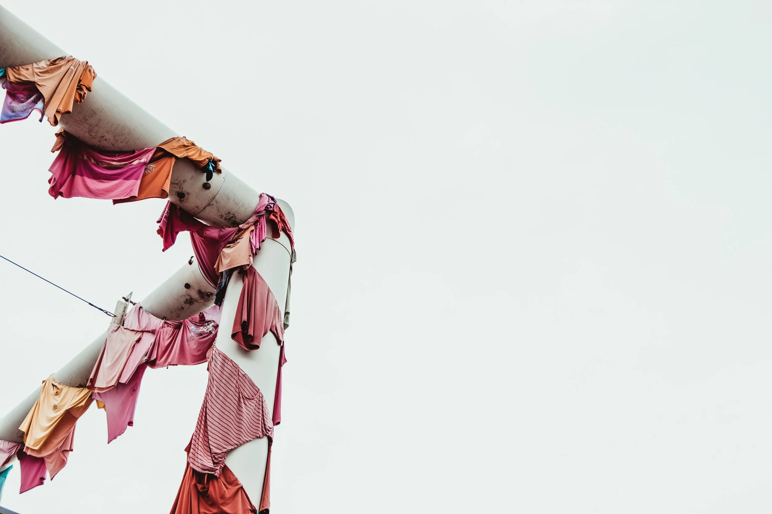 Clotheslines of pastel pink and orange clothing draped over gray industrial poles.