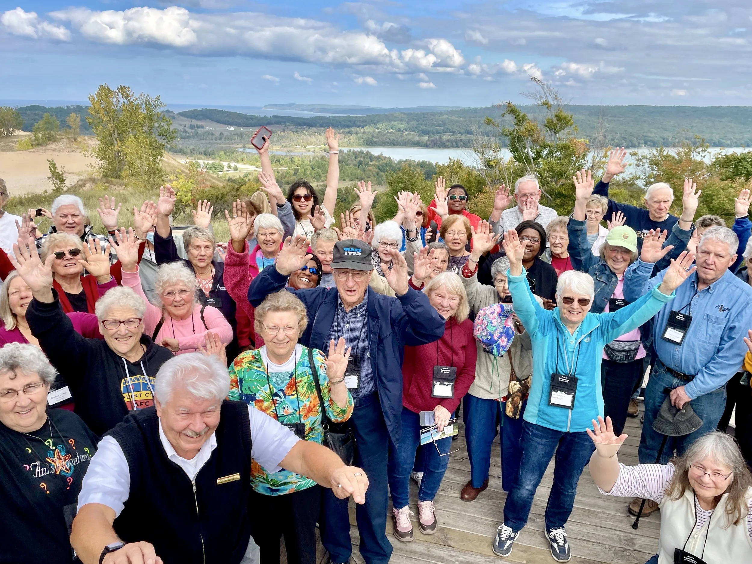 Group of travelers displaying excitement with the iconic dune landscape of Sleeping Bear Dunes in the distance.