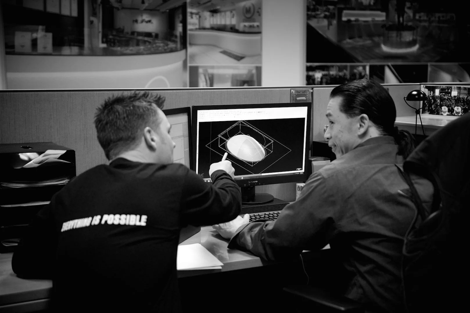 Two men working together at a computer in an office, examining a 3D model on the monitor.