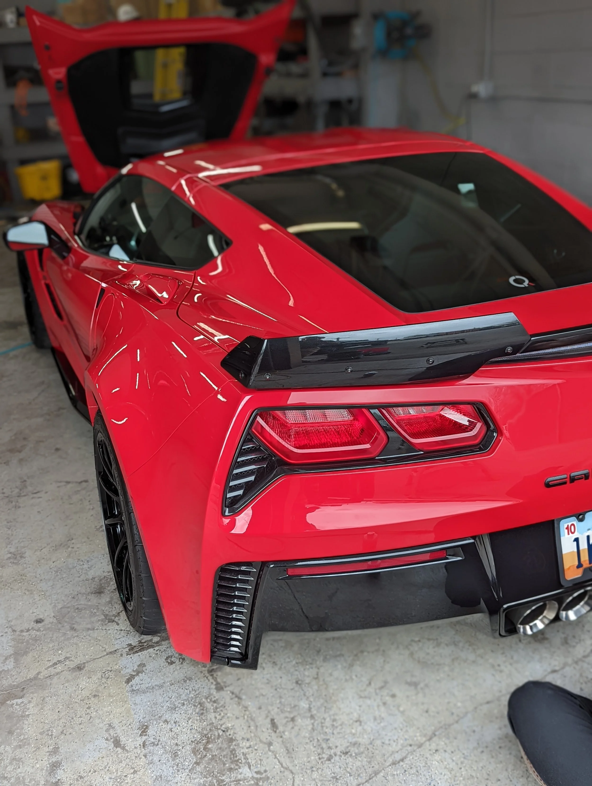 Red sports car with Wild Detail, open rear hatch, in a garage or workshop setting.