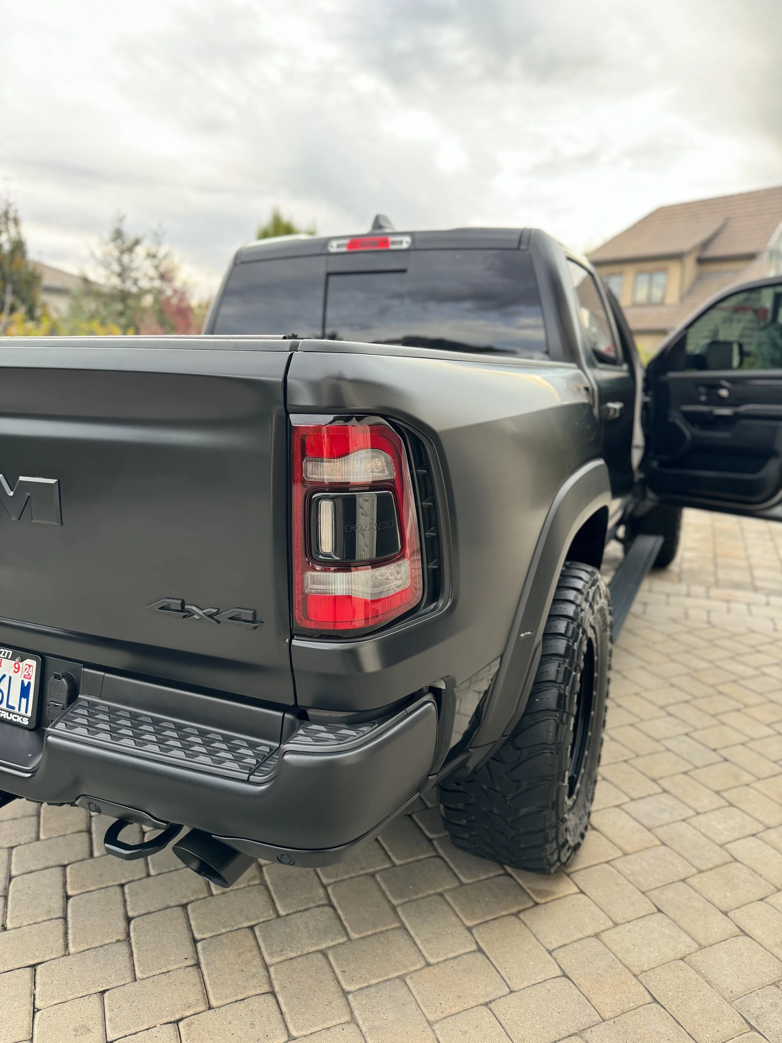 Black pickup truck with Wild Detail parked on a brick driveway with an open passenger door and cloudy sky.