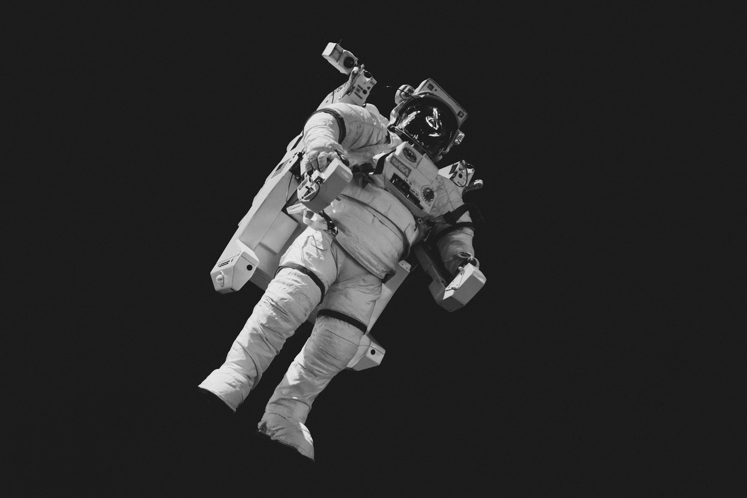 Black and white photo of an astronaut in a spacesuit floating in space against a dark background.