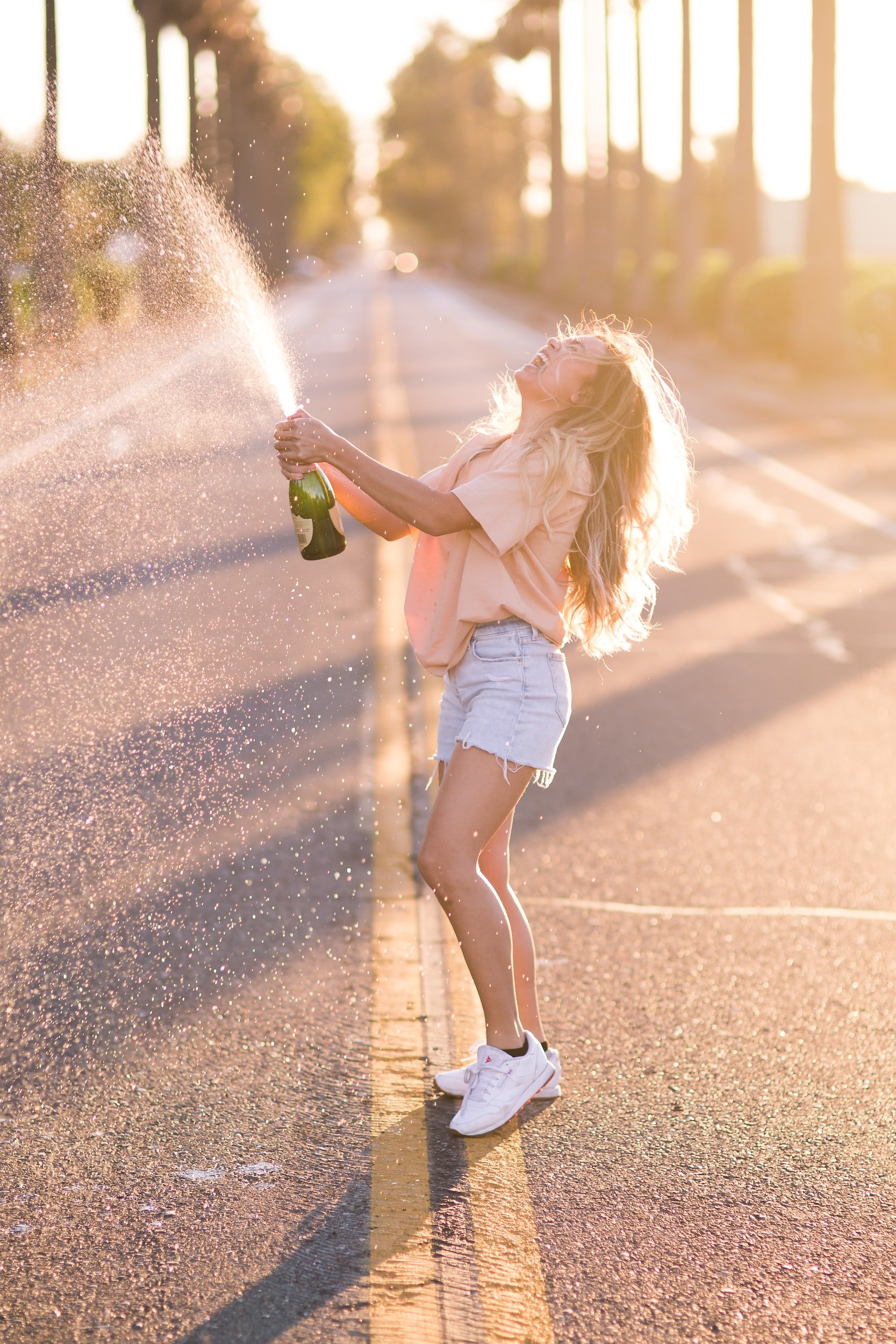 Girl standing in the middle of the road shaking a bottle of champagne