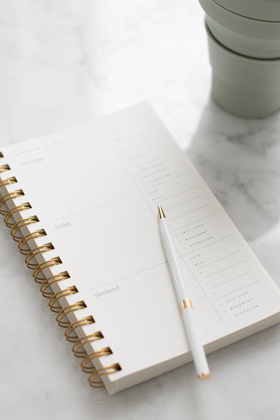 Weekly planner sitting on marble counter with coffee mug and pen