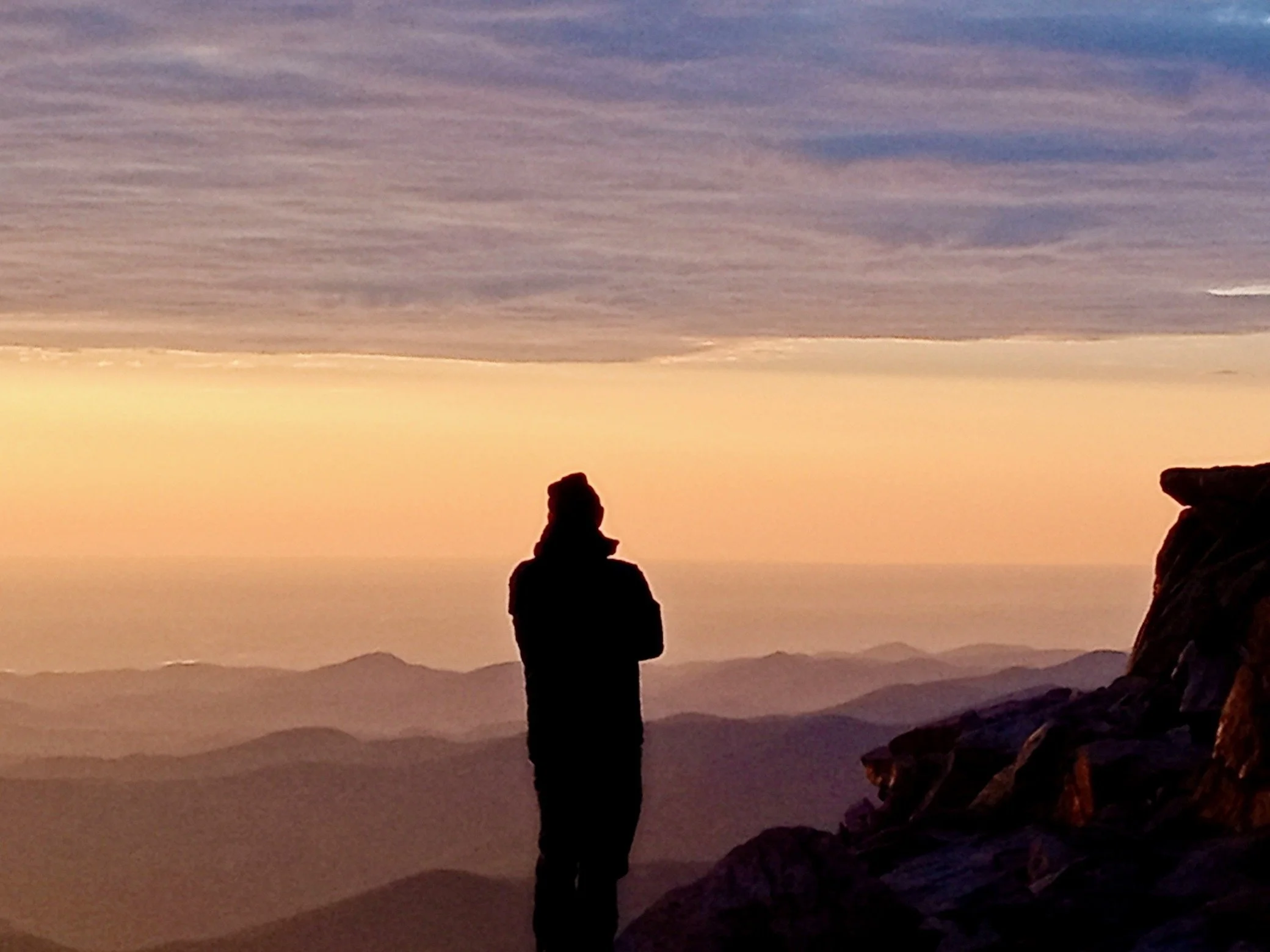 Silhouette of person on mountain at sunrise with expansive view